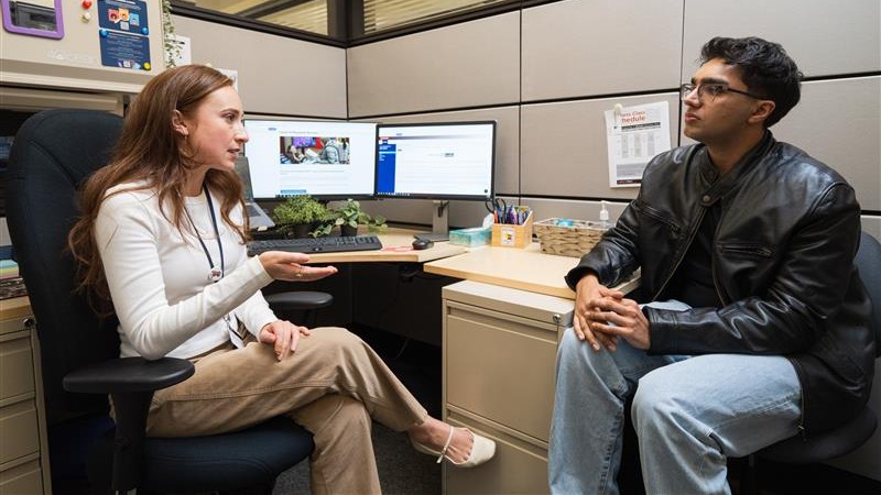 A Field Placement Coordinator sits by a desk speaking to a male student sitting across from her