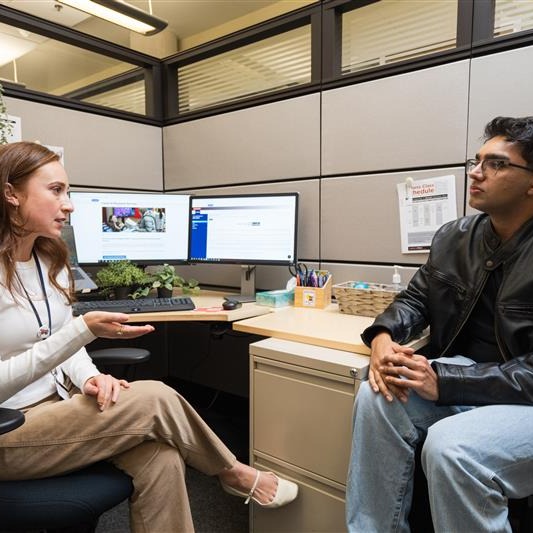 A Field Placement Coordinator sits by a desk speaking to a male student sitting across from her