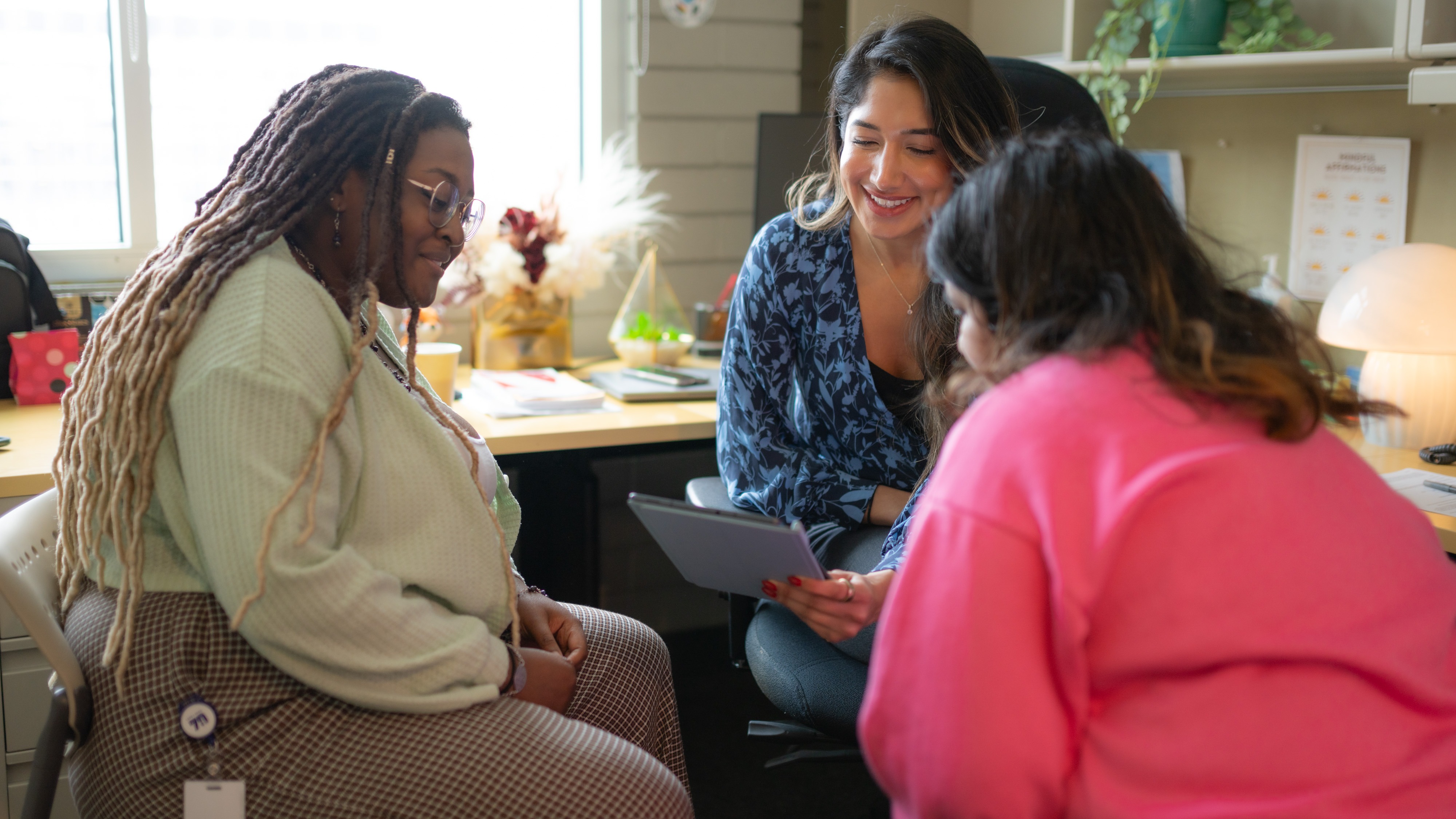 Three people gather around a tablet while seated