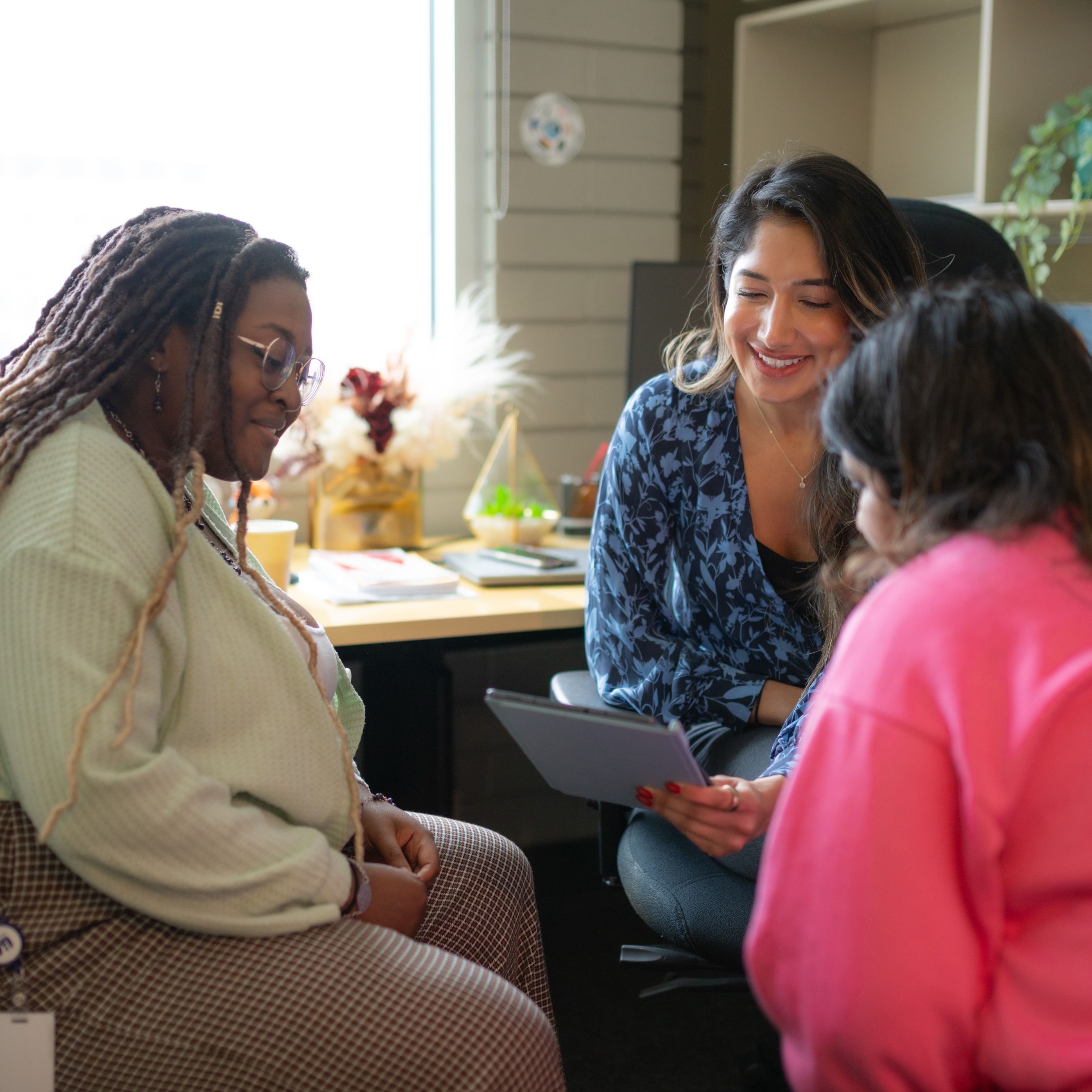 Three people gather around a tablet while seated