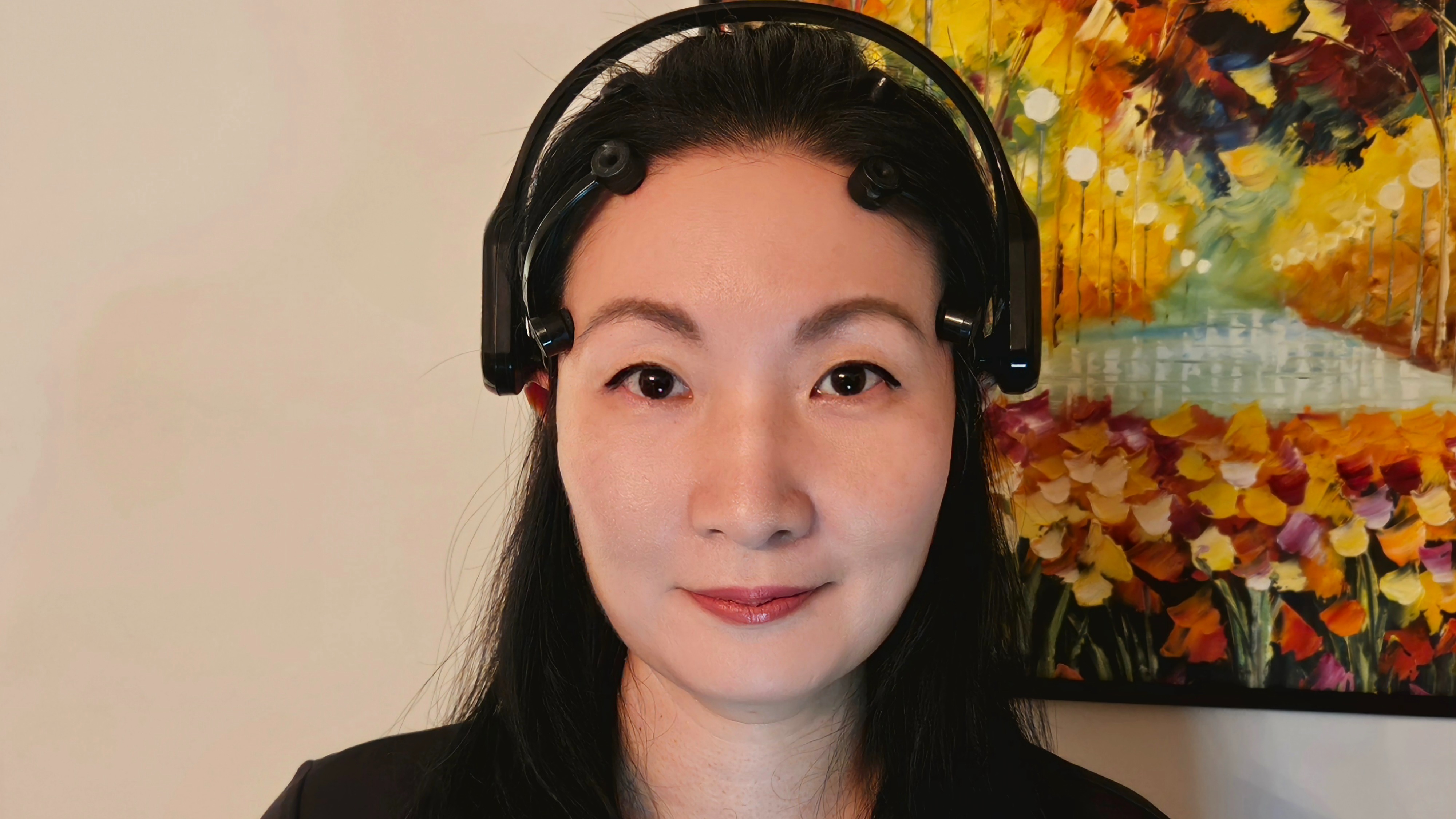 Dr. Alice Kim poses in front of a painting wearing a black EEG headset