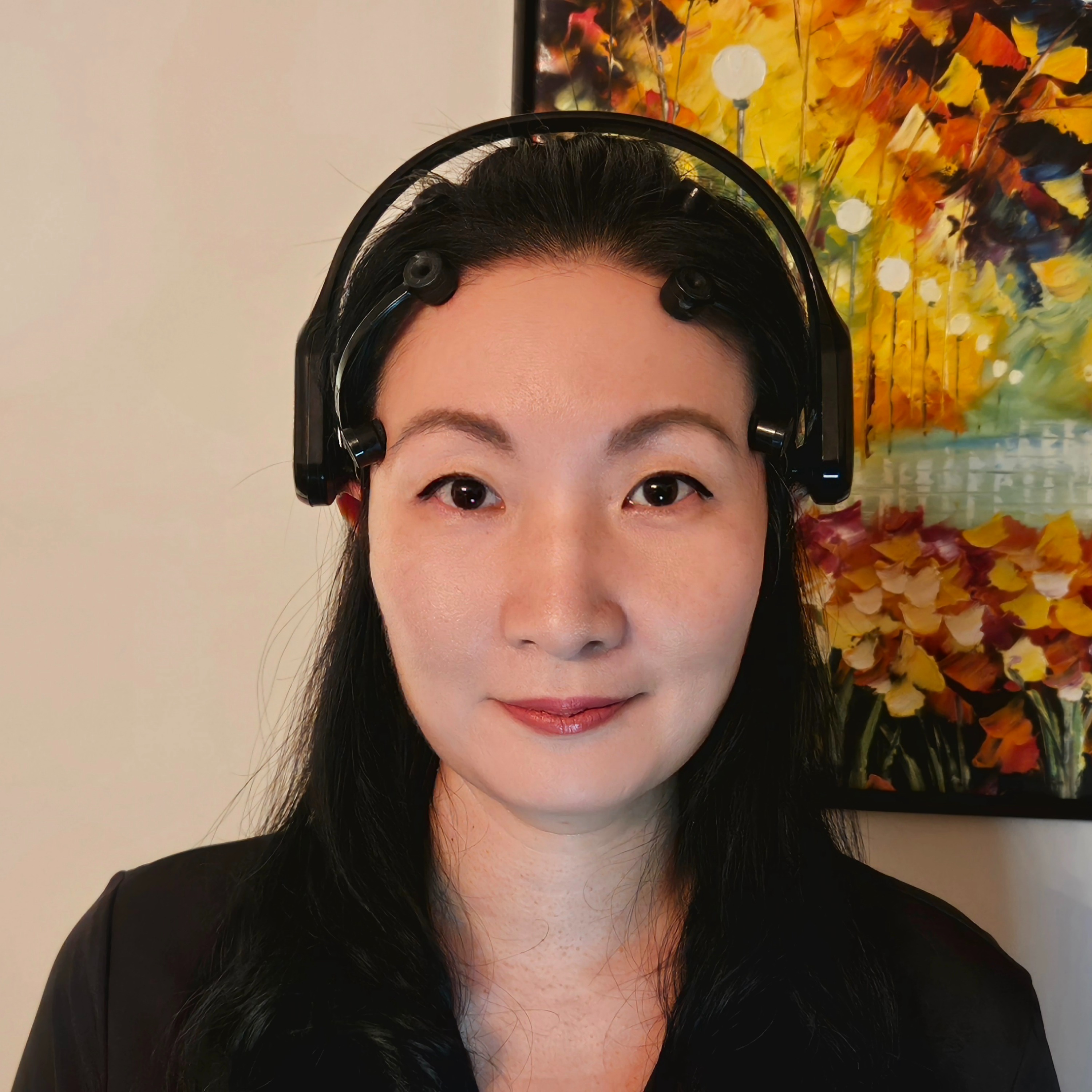 Dr. Alice Kim poses in front of a painting wearing a black EEG headset