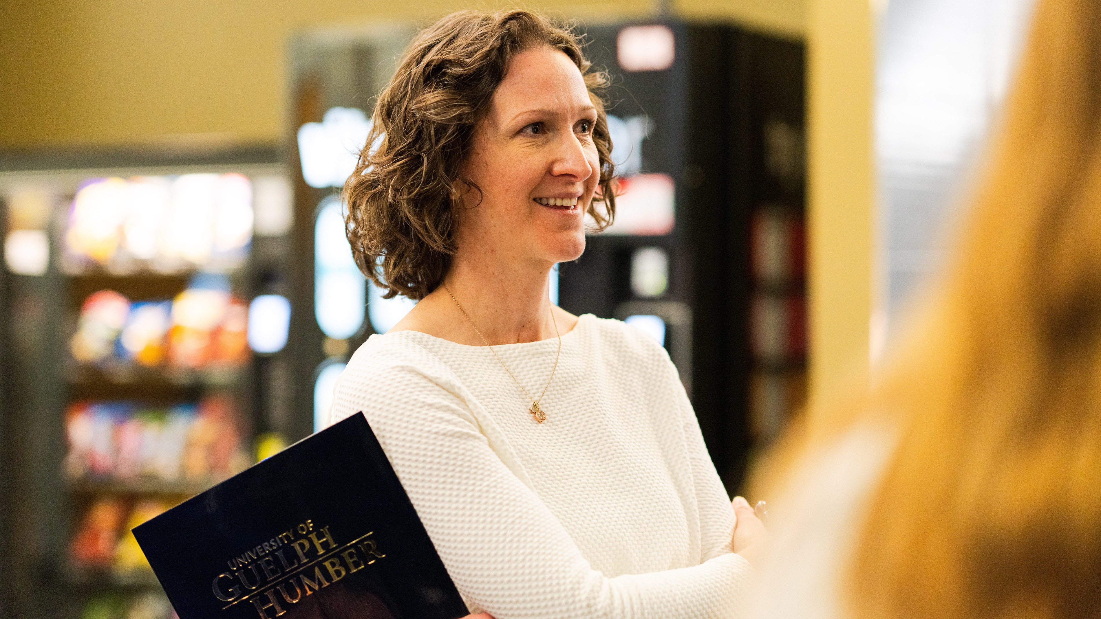 Dr. Leslie Auger wears a white top while holding a University of Guelph-Humber folder, looking to the side