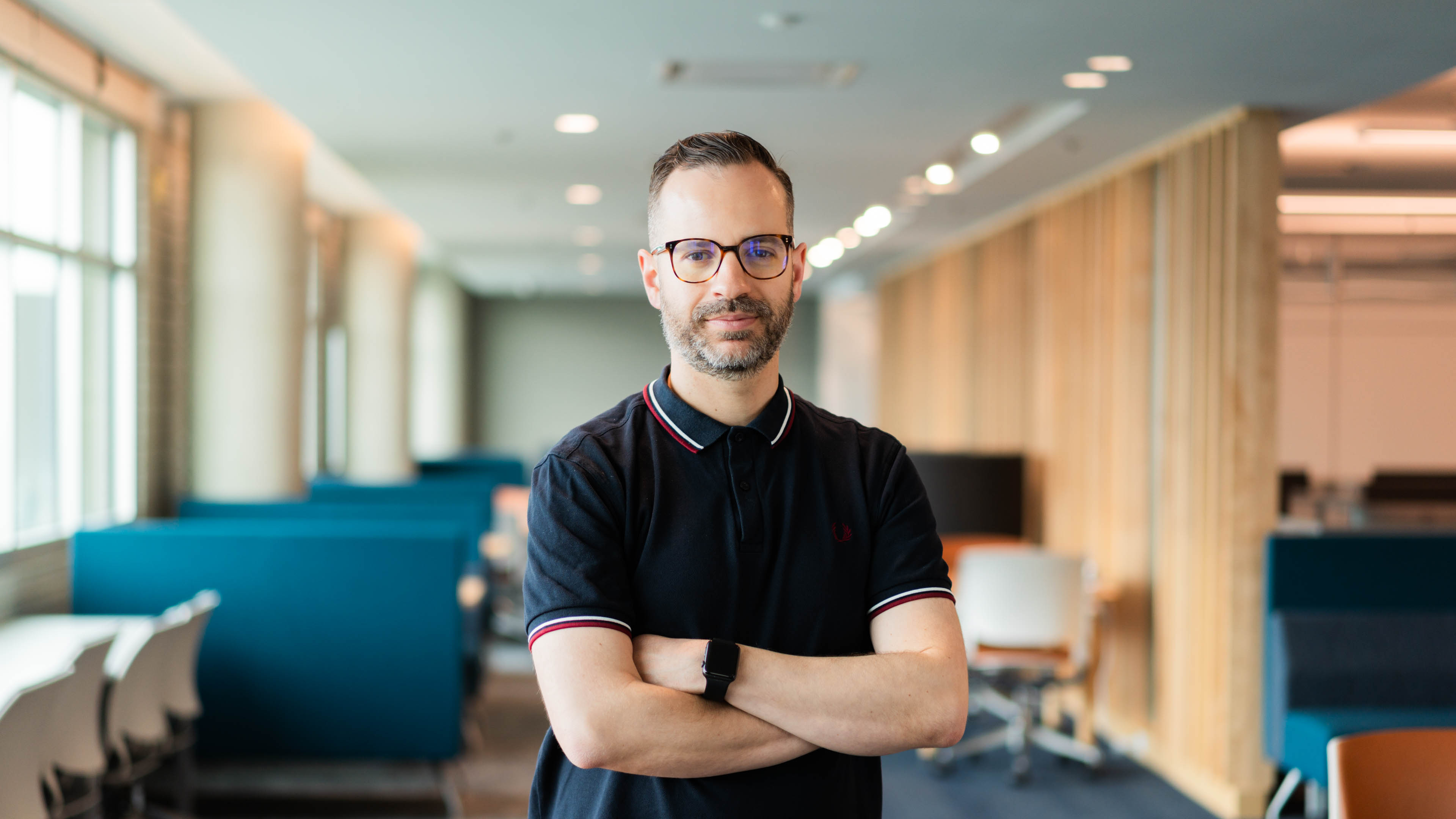 Marc Tavares poses with his arms crossed over is torso in front of blue and beige chairs