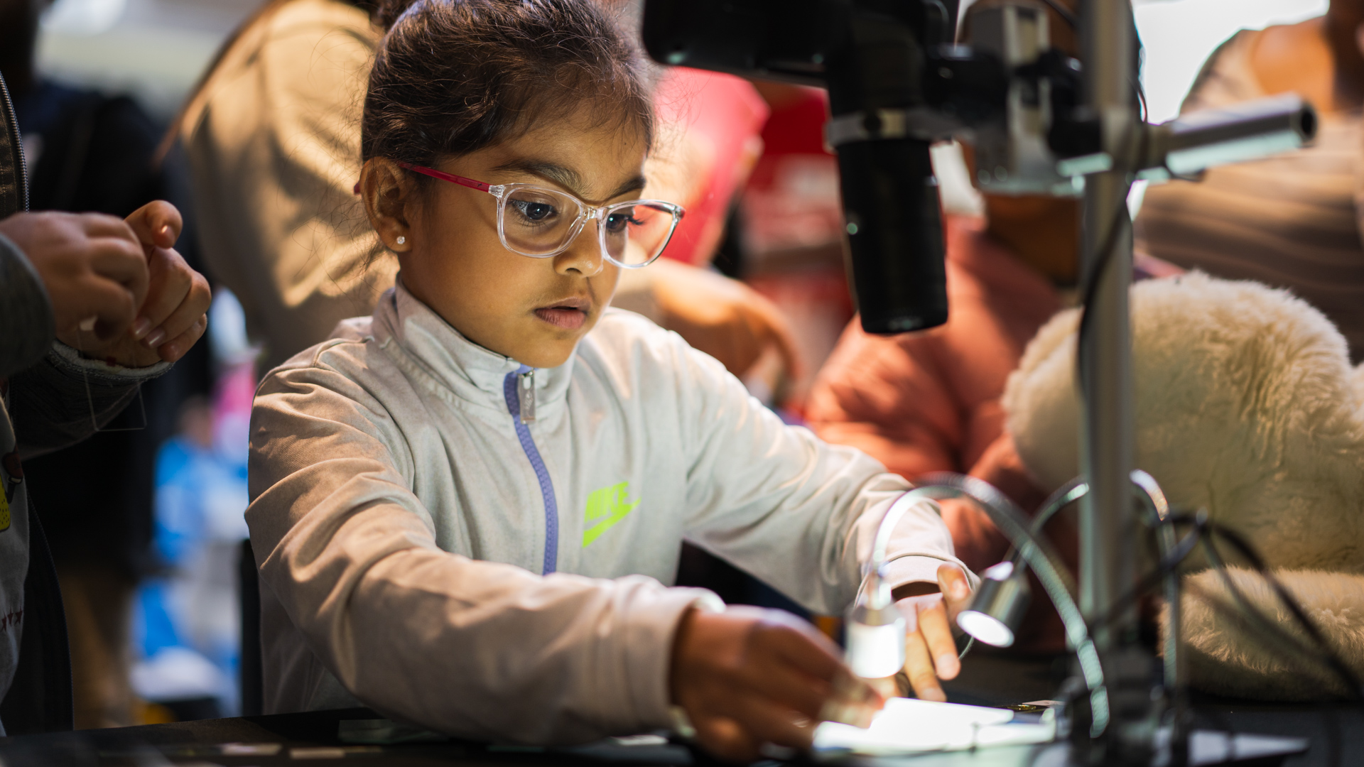 A child with glasses is illuminated by a light from a microscope at Science Rendezvous at the University of Guelph-Humber