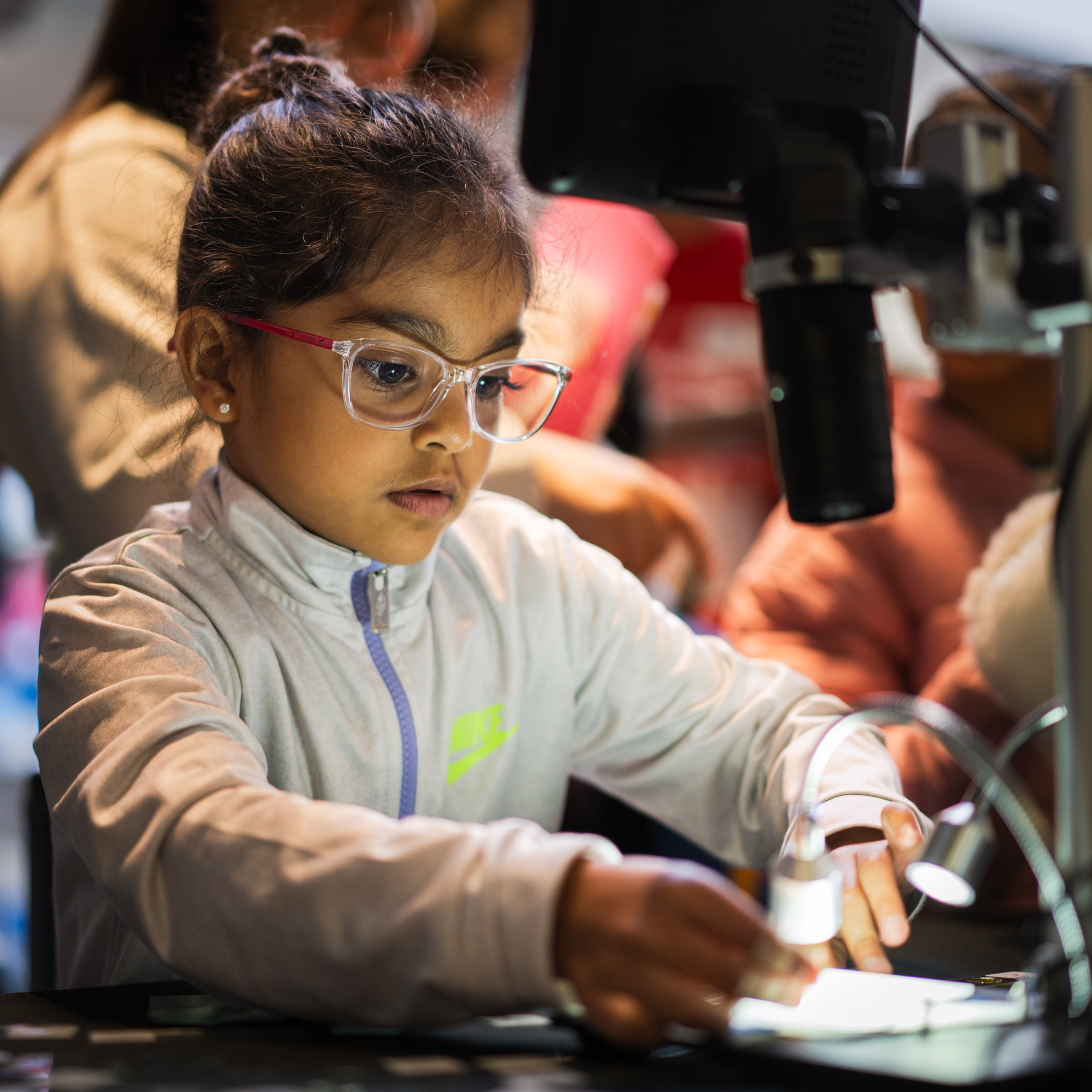 A child with glasses is illuminated by a light from a microscope at Science Rendezvous at the University of Guelph-Humber
