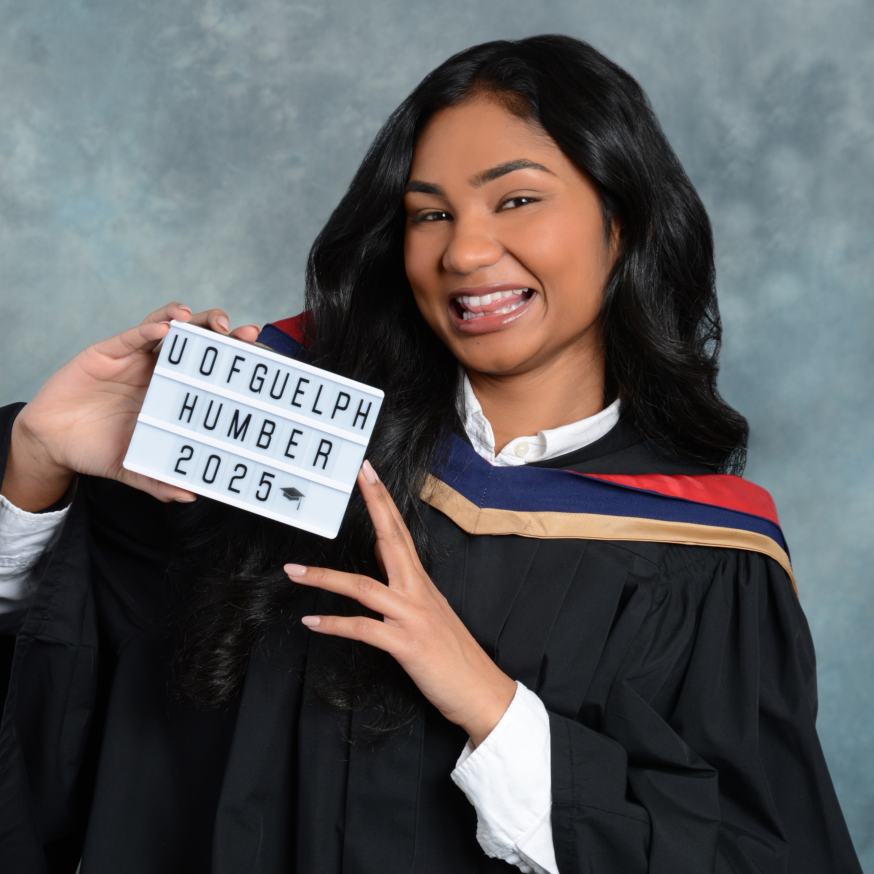 Naisha Suthaharan wears a graduation robe and holds a sign that says U of Guelph-Humber 2025