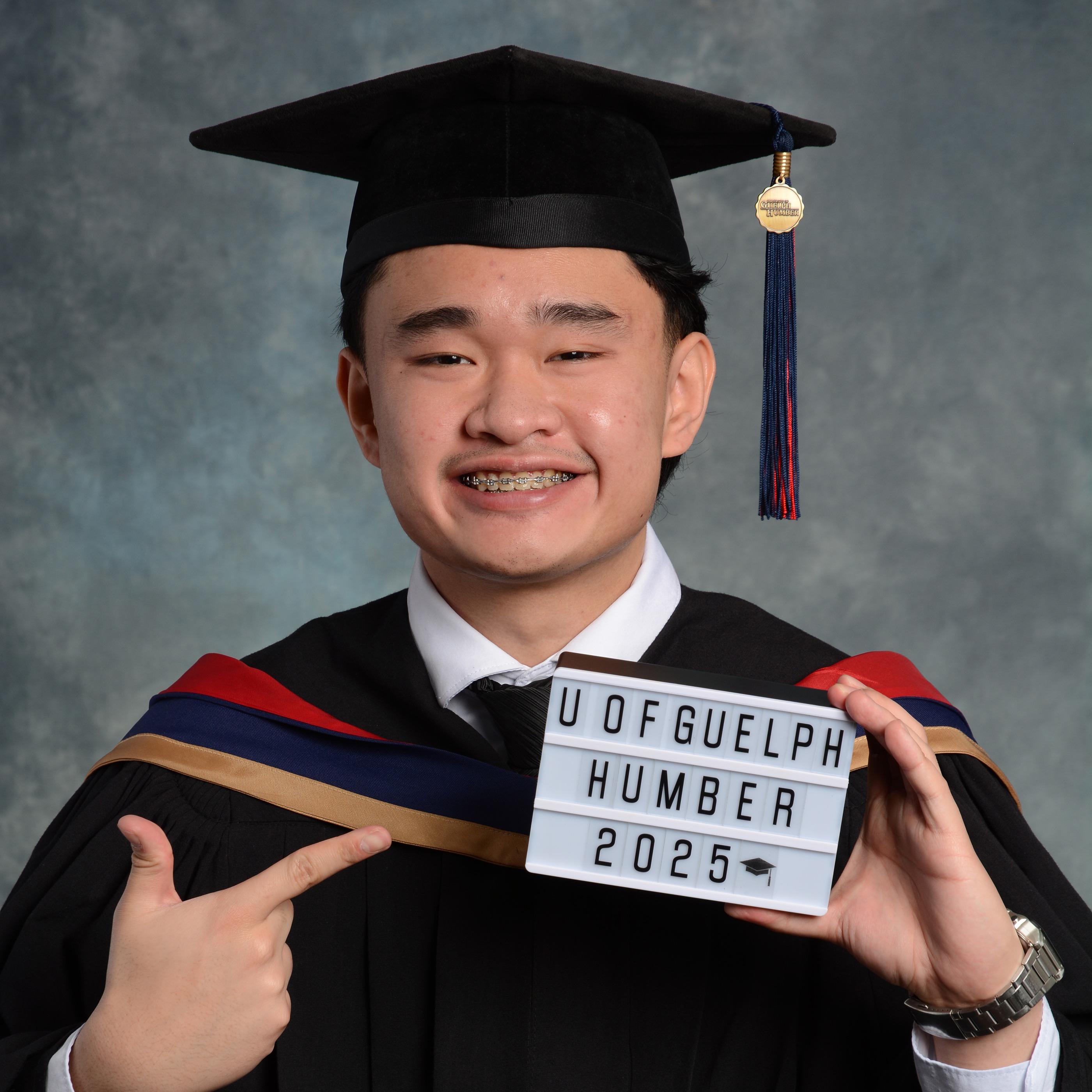 Yul is wearing a graduation gown and holding up a sign that says U of Guelph-Humber 2025