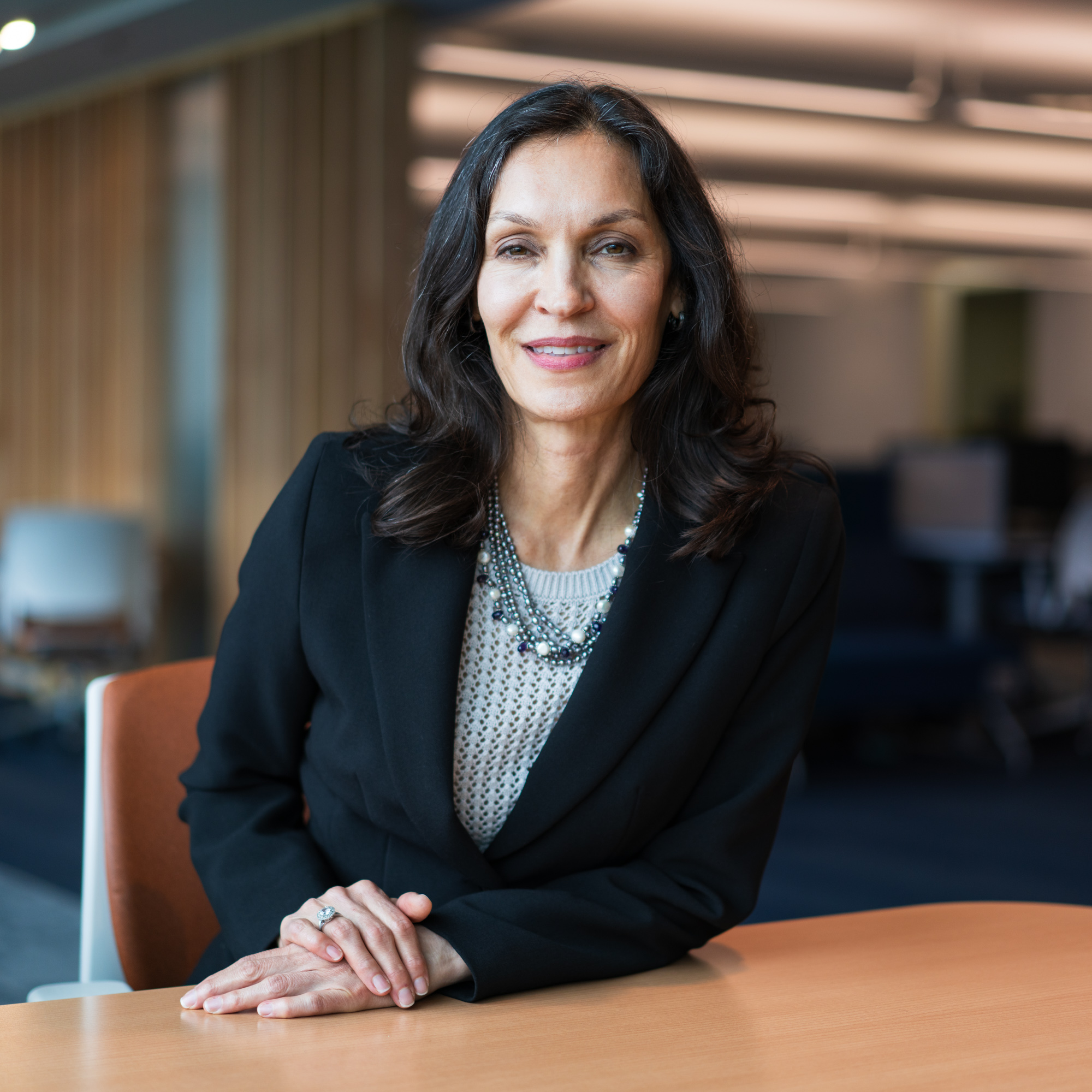 Ann Wallington wears a black blazer and sits in an orange chair