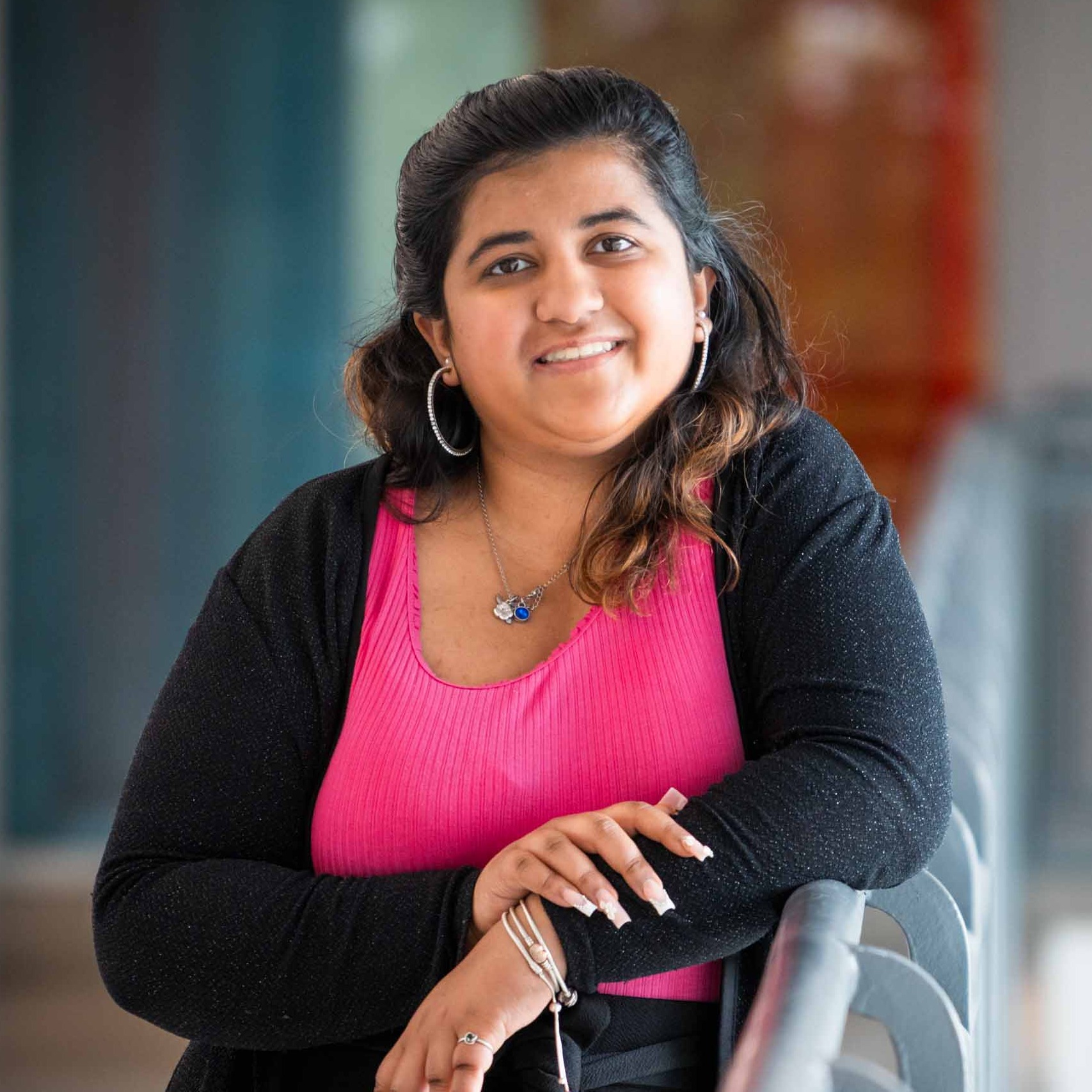 Nandita leans against a hand rail, wearing a bright pink top and black sweater