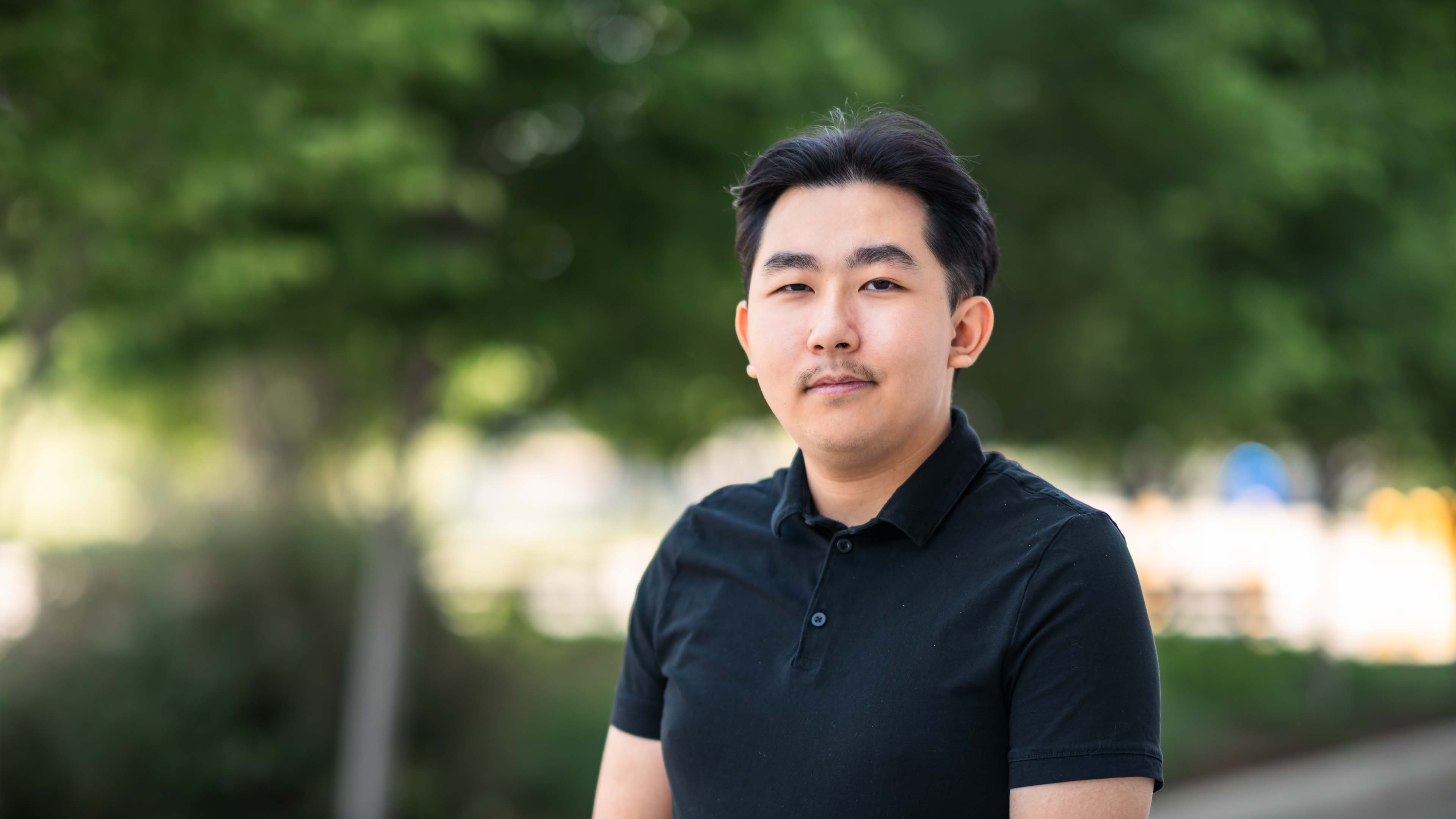 Tin Dao stands in front of blurred trees while wearing a black shirt
