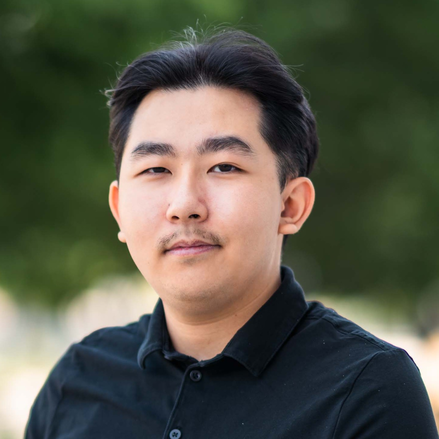 Tin Dao stands in front of blurred trees while wearing a black shirt