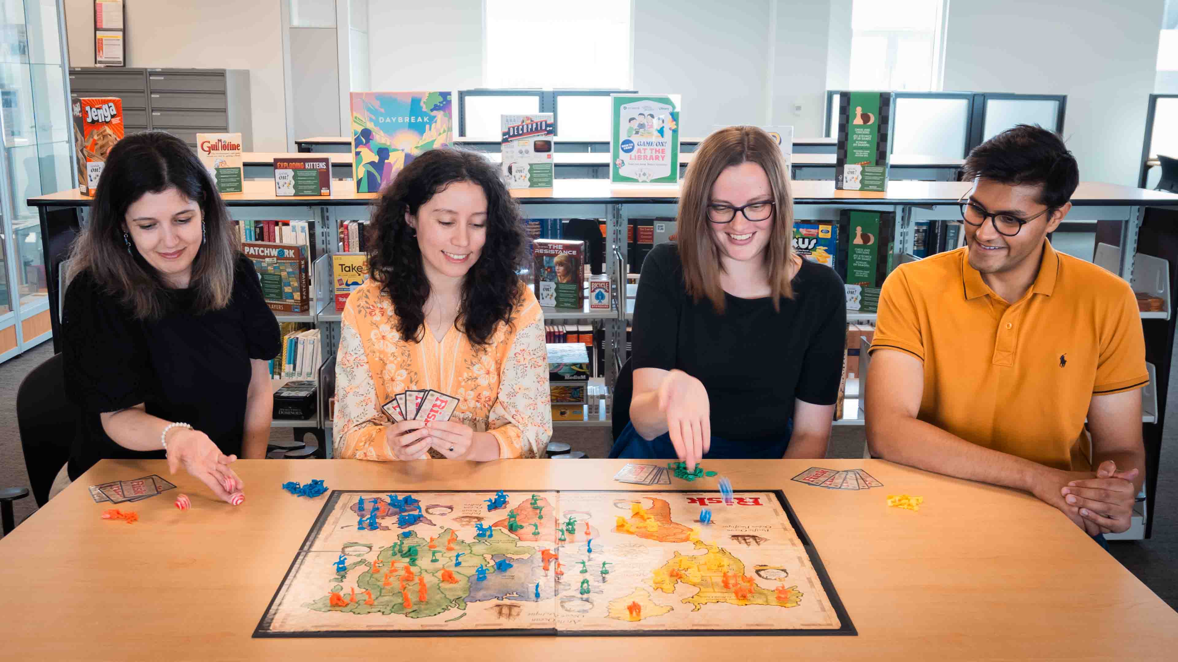 Four people sit at a table playing a board game at the library