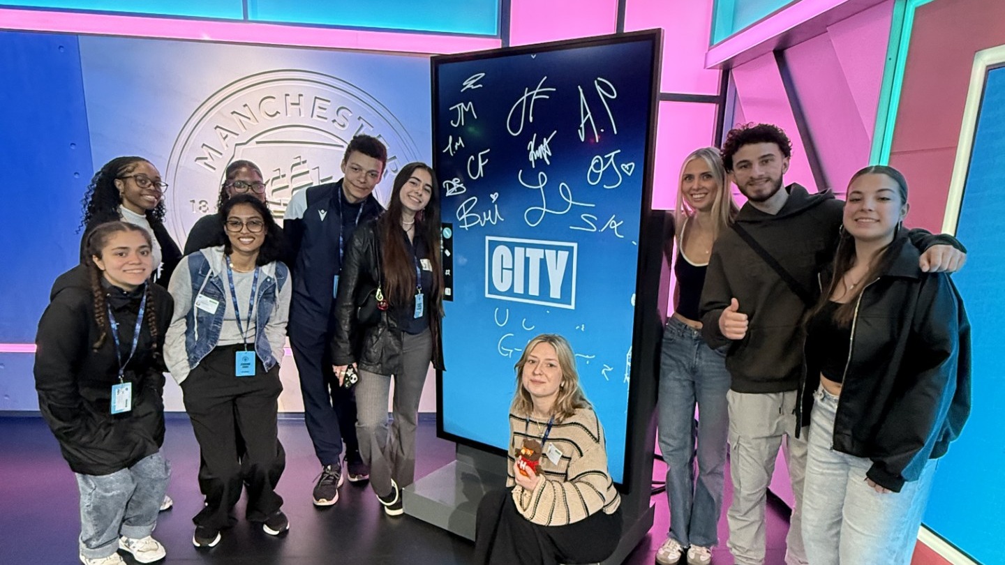 A group of students pose in front of a tall screen in Studio 1