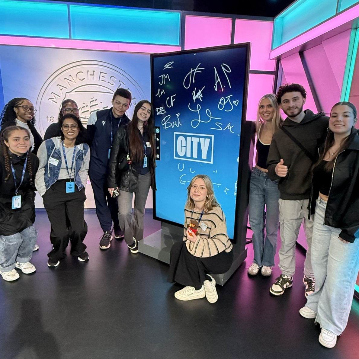 A group of students pose in front of a tall screen in Studio 1