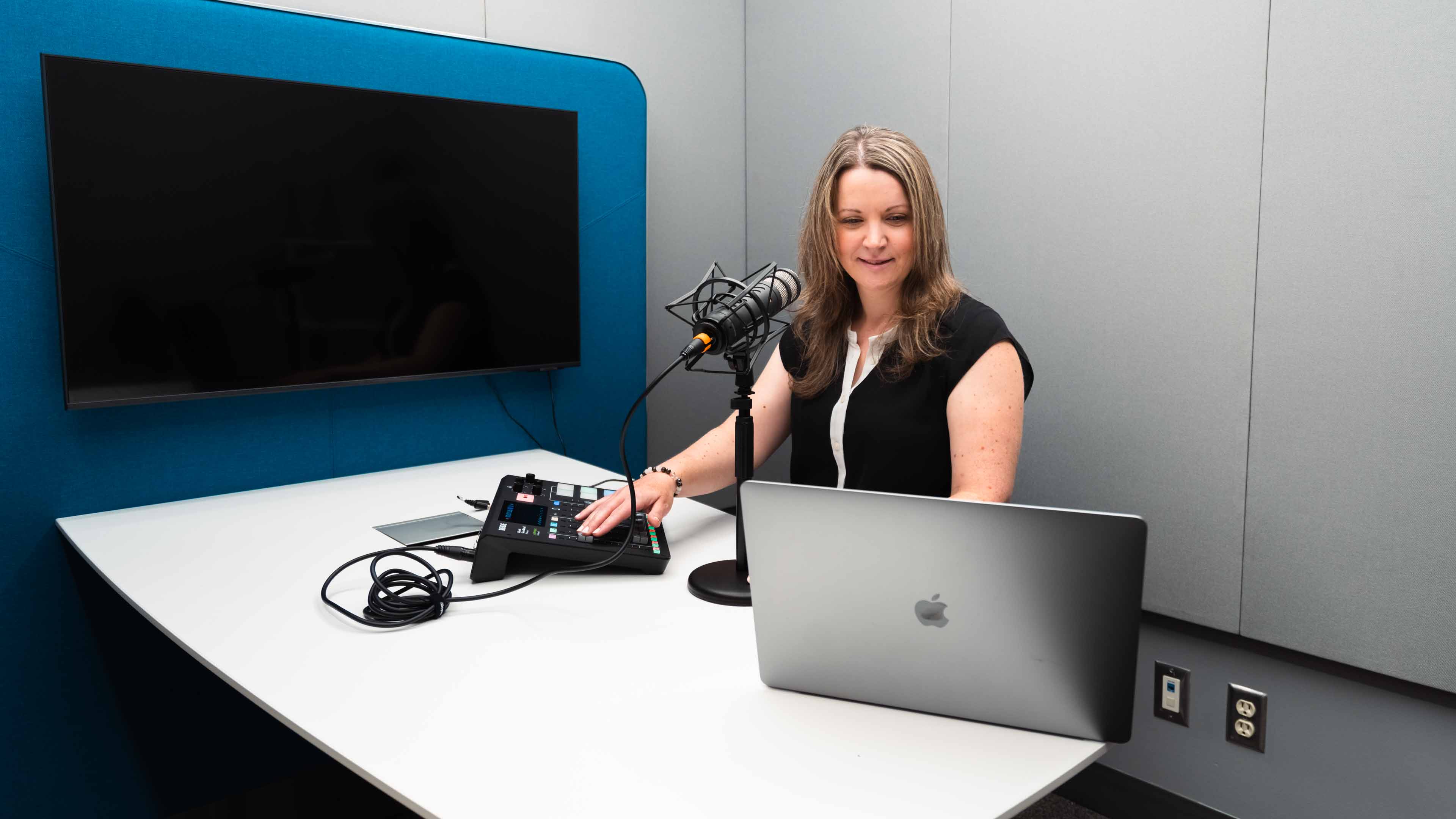 Katie Begley sits in front of a microphone and a laptop as she records her podcast