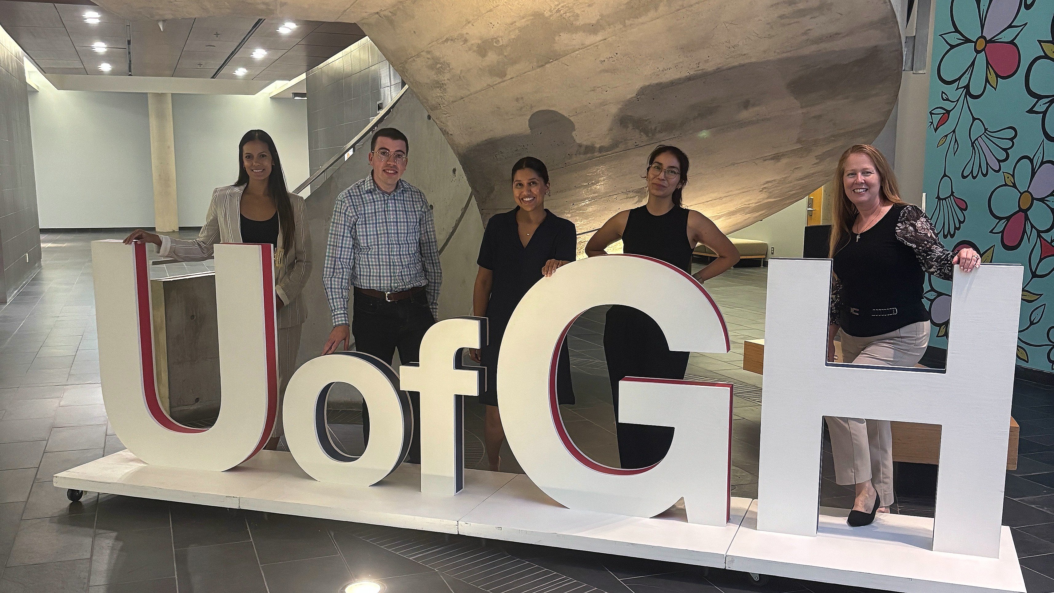Alumni Ambassador Council members stand behind the giant U of GH letters under the spiral staircase in the atrium