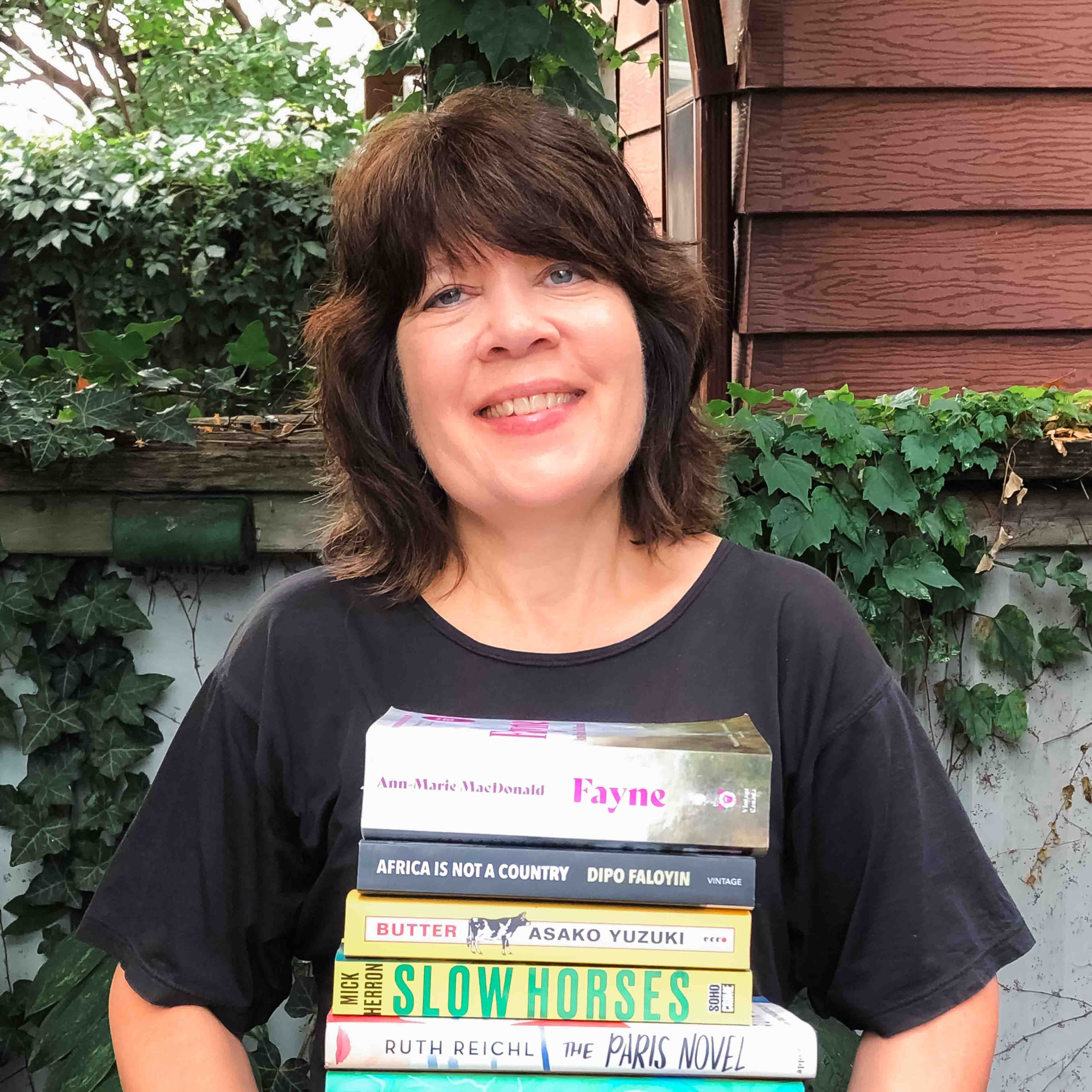 Sue Hunter holds a stack of books, smiling