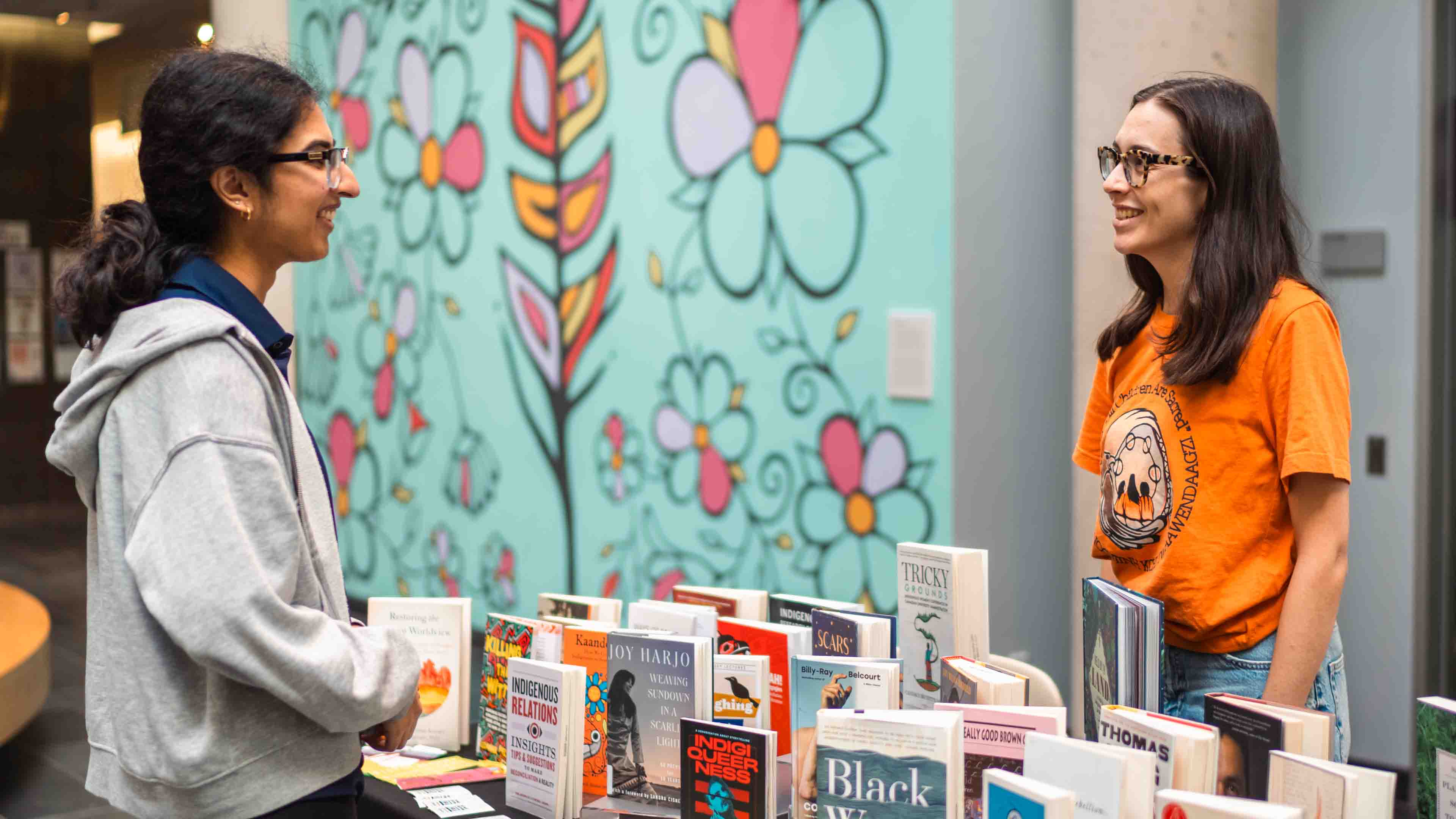 student at table with library books speaking with other student