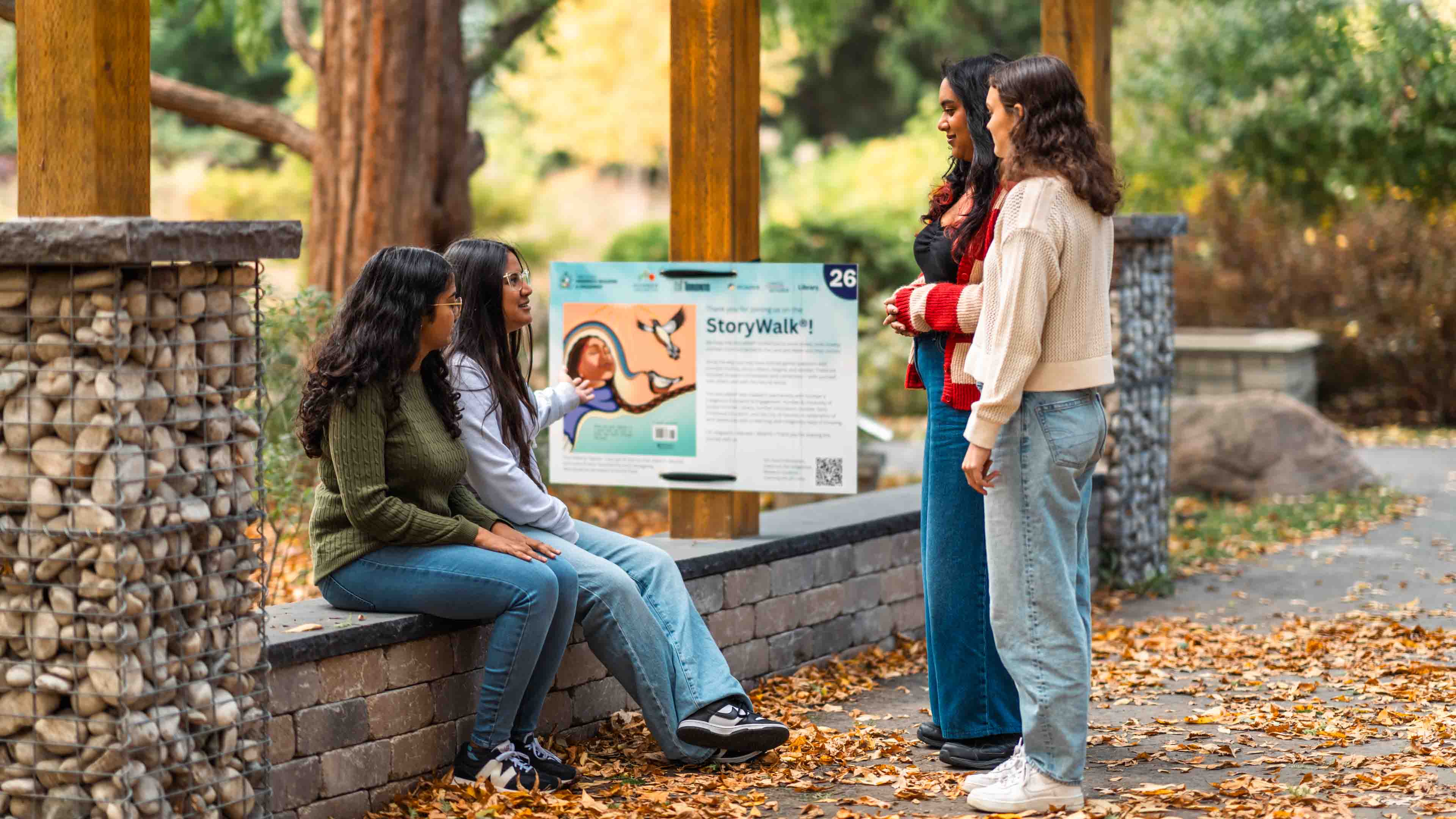 Four students look at a StoryWalk poster in the Humber Arboretum amongst nature