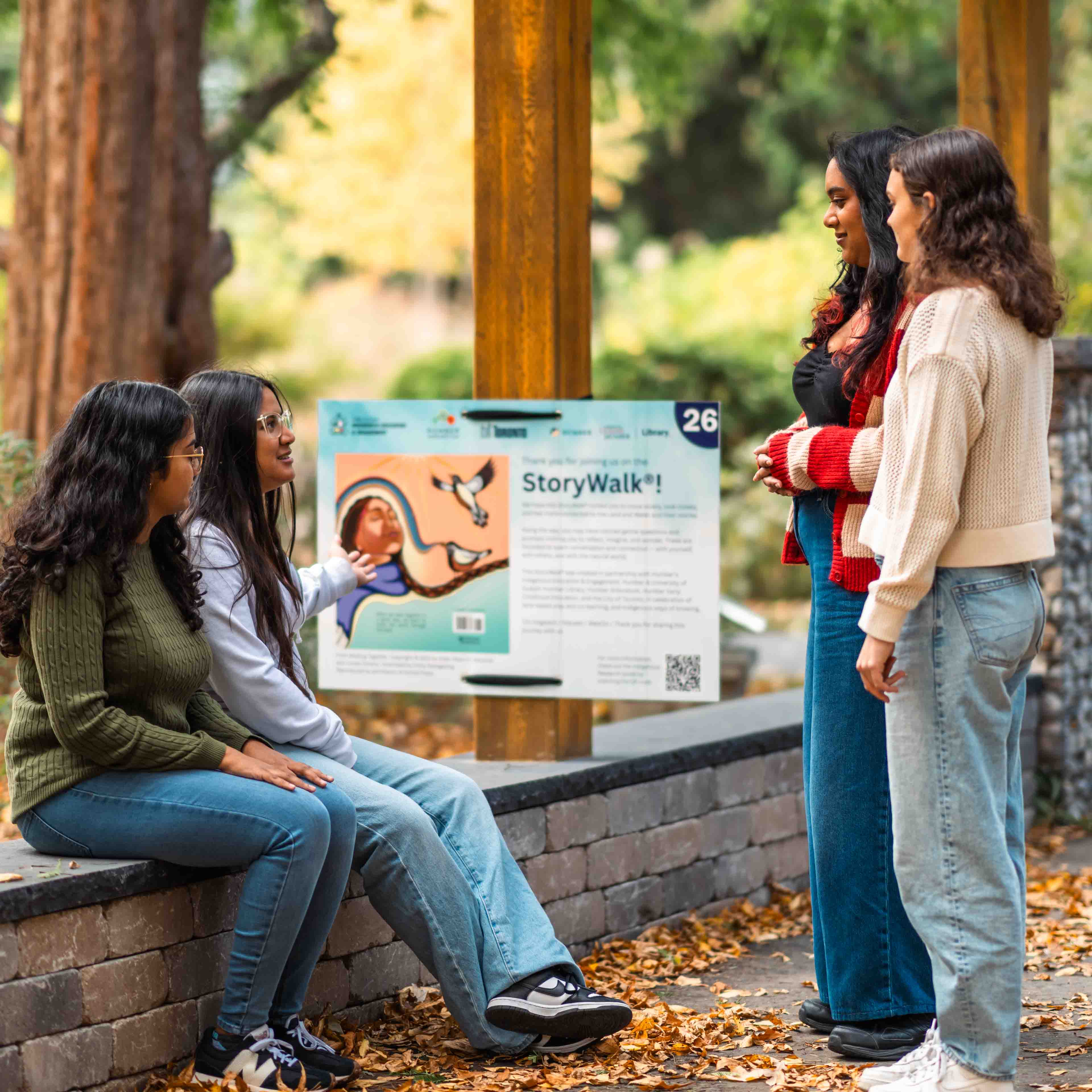 Four students look at a StoryWalk poster in the Humber Arboretum amongst nature