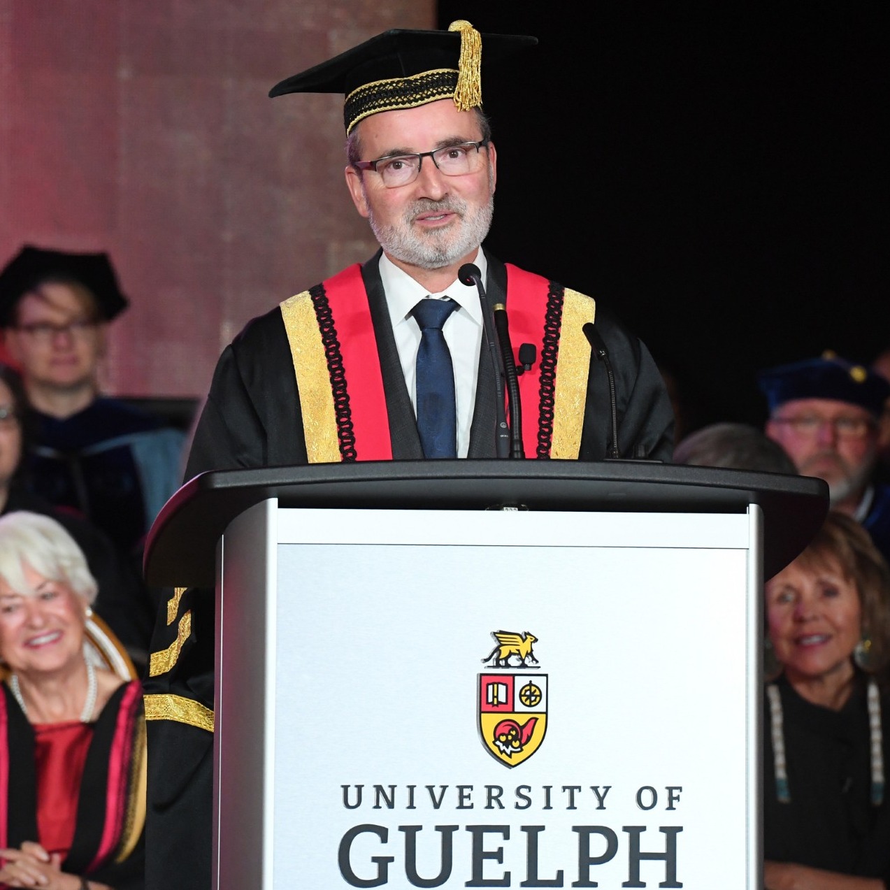 Dr. Van Acker speaks at a podium in academic regalia