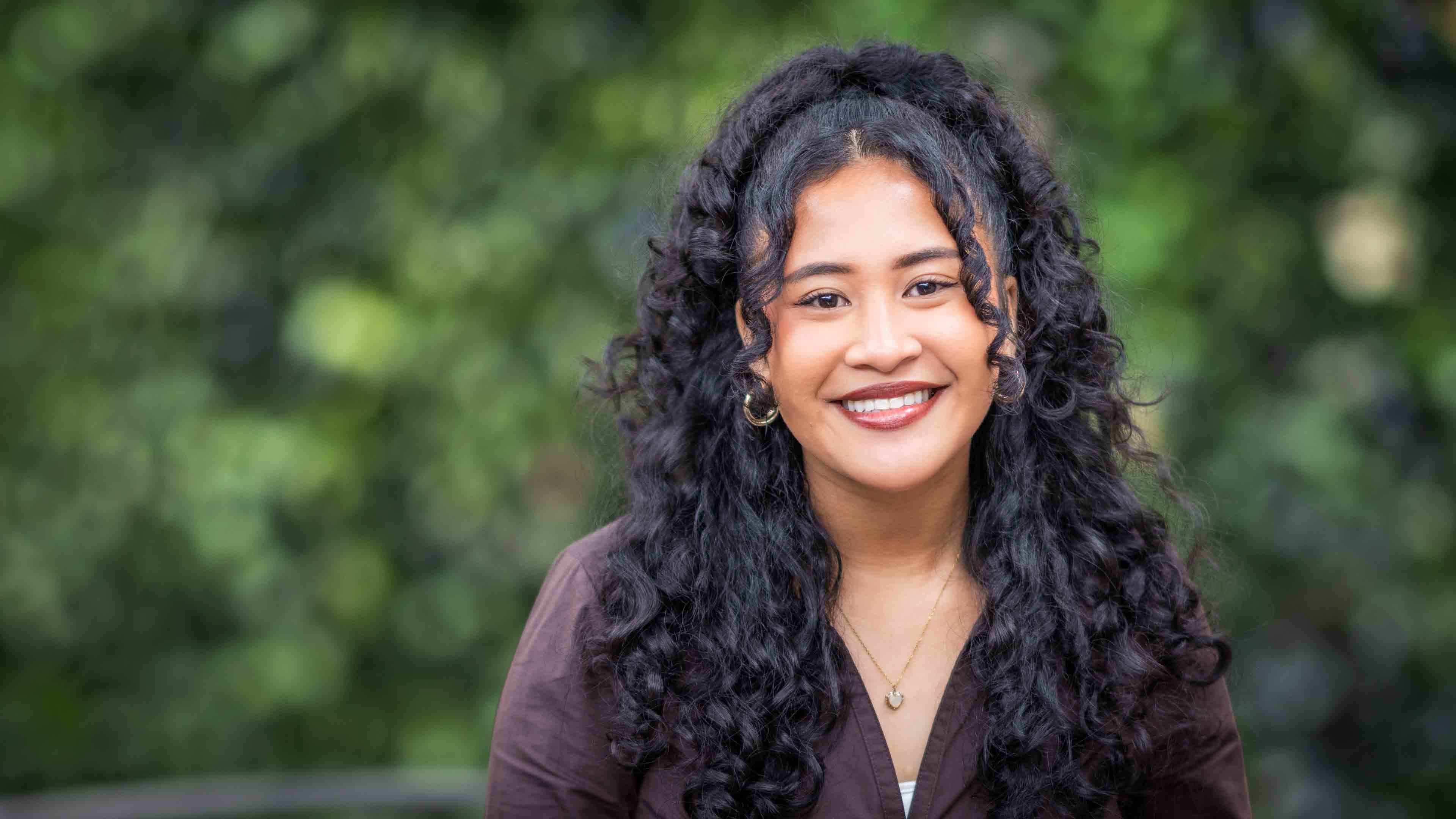 Rachel Balintec smiles for the camera in front of a green plant wall