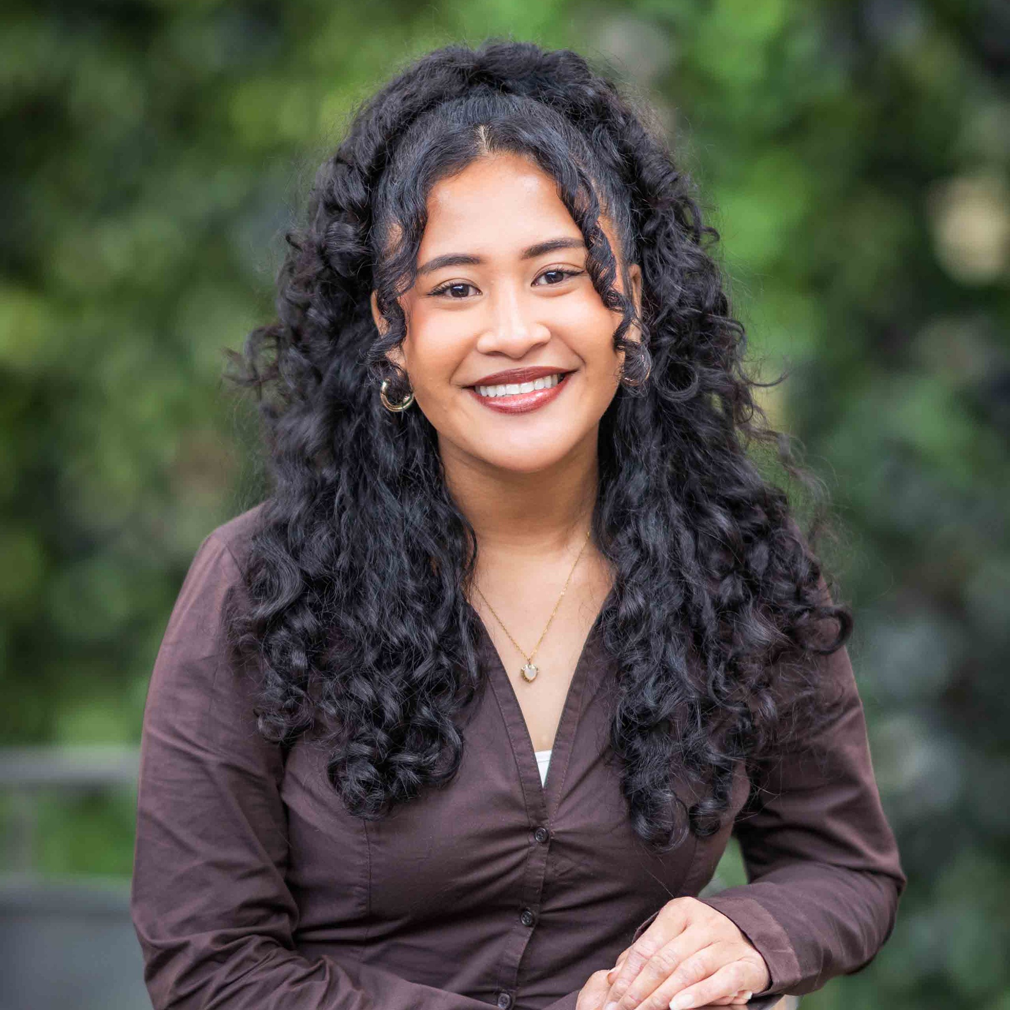 Rachel Balintec smiles for the camera in front of a green plant wall