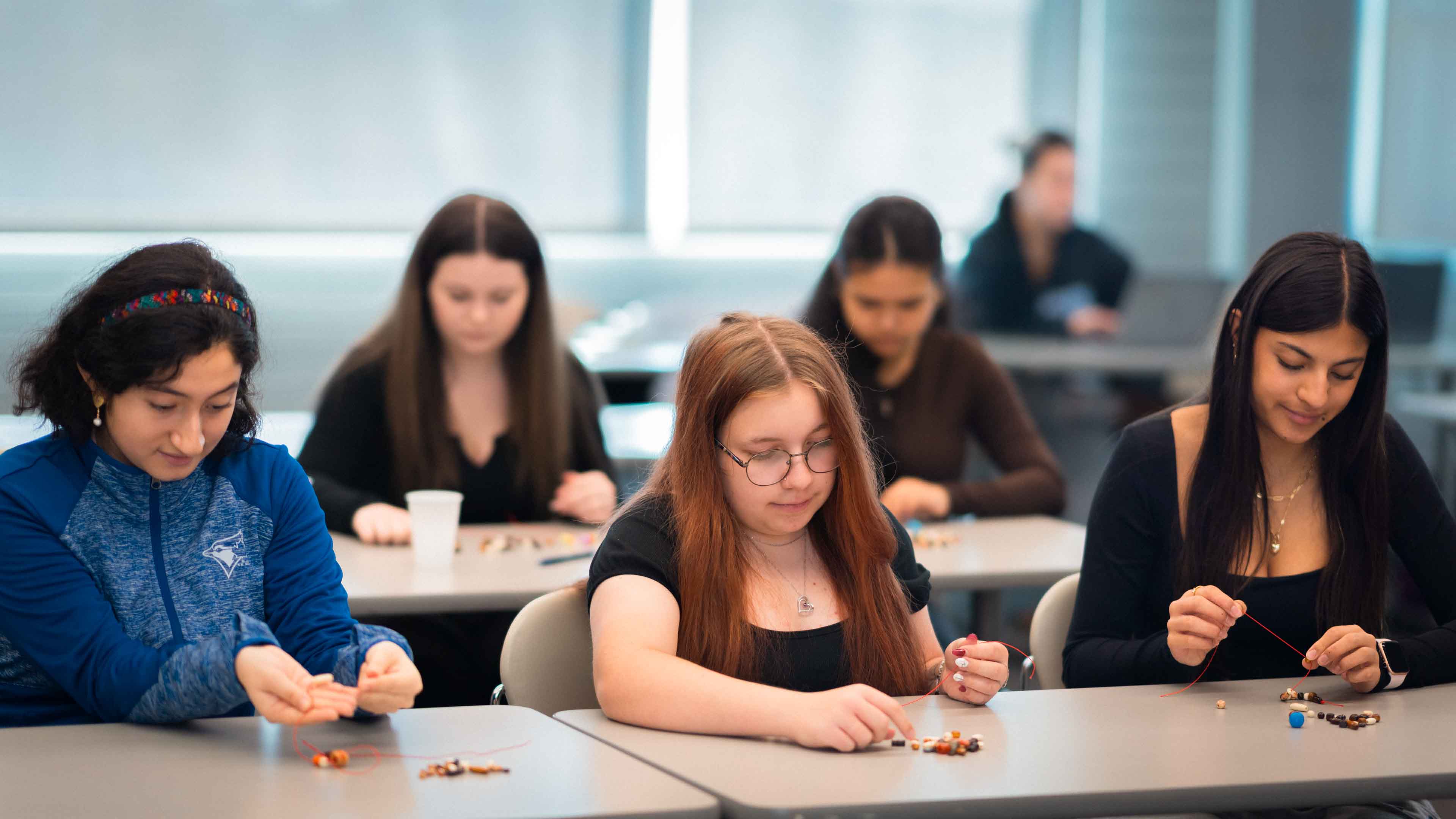 Students put beads onto a string to make knowledge necklaces