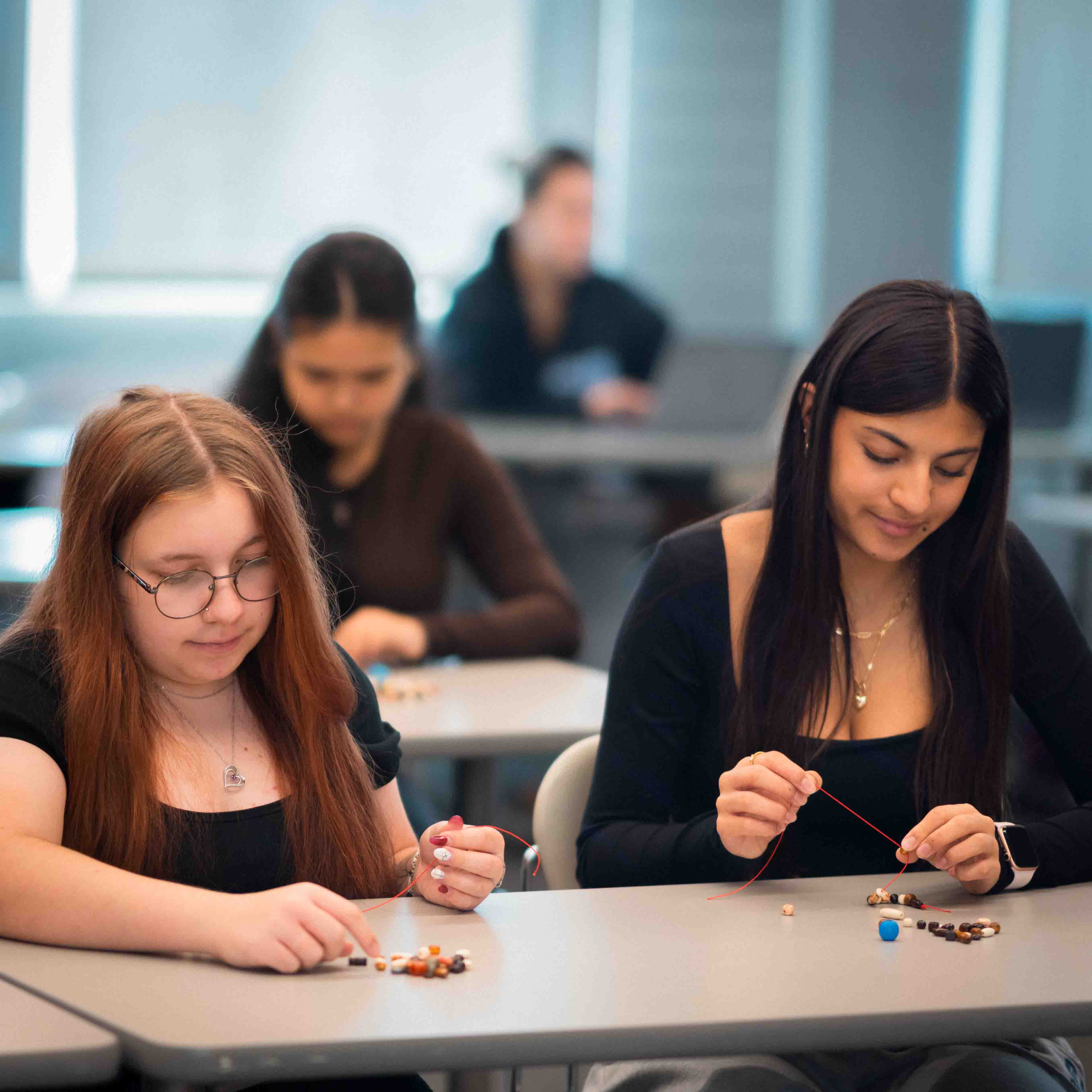 Students put beads onto a string to make knowledge necklaces