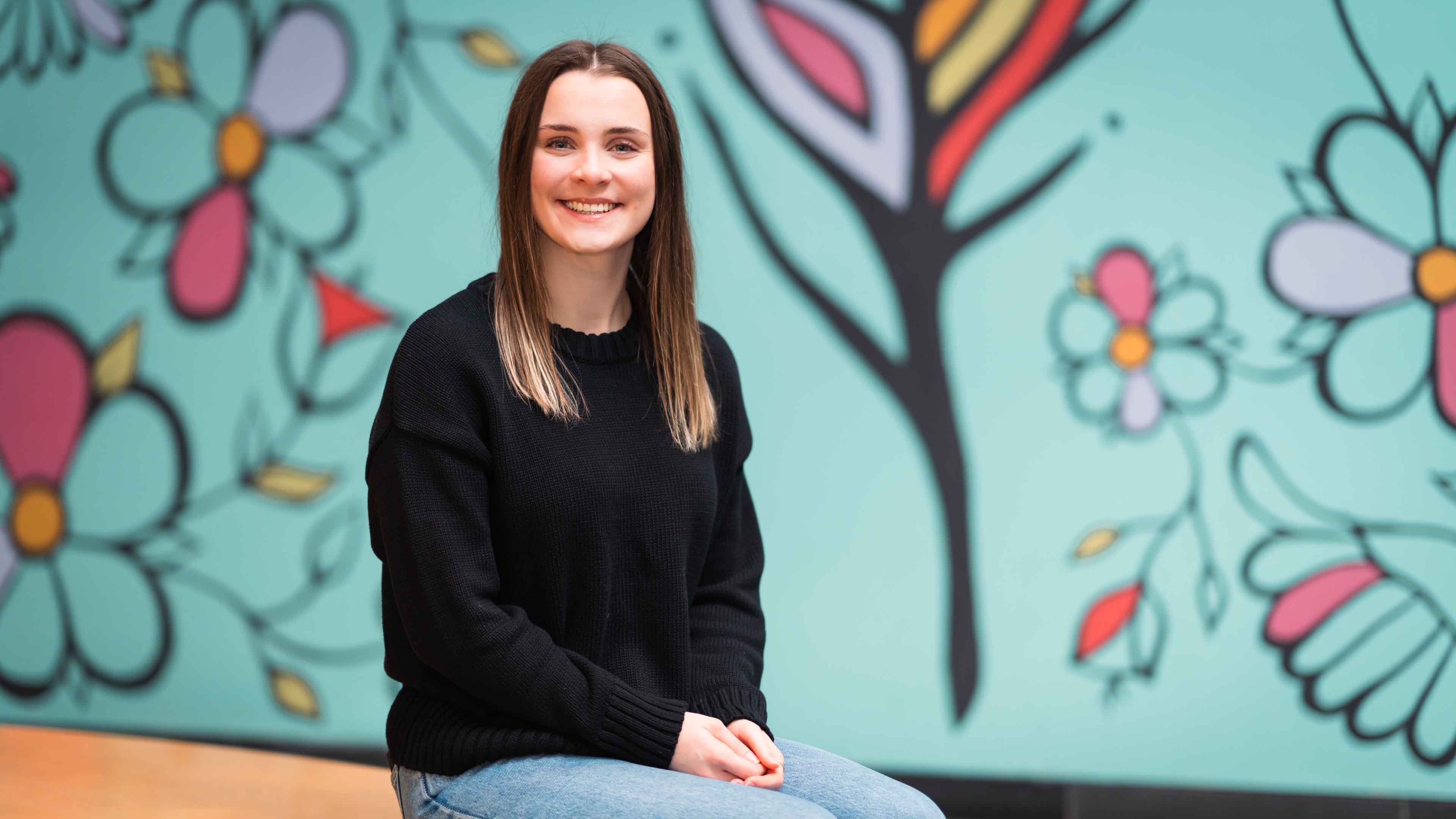 Veronica Wood sits in front of a turquoise mural at Guelph-Humber