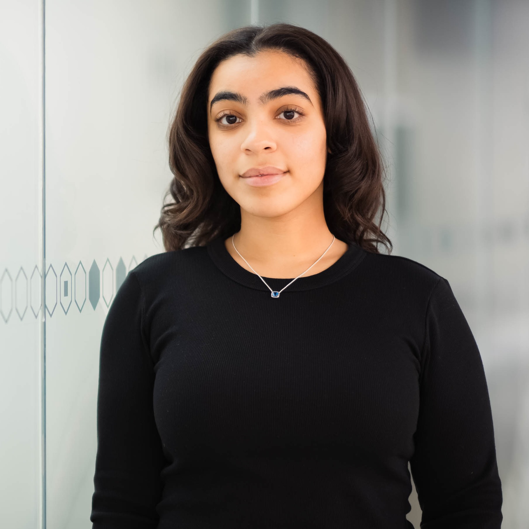Tara Mohammad stands in front of a glass wall, wearing a black shirt