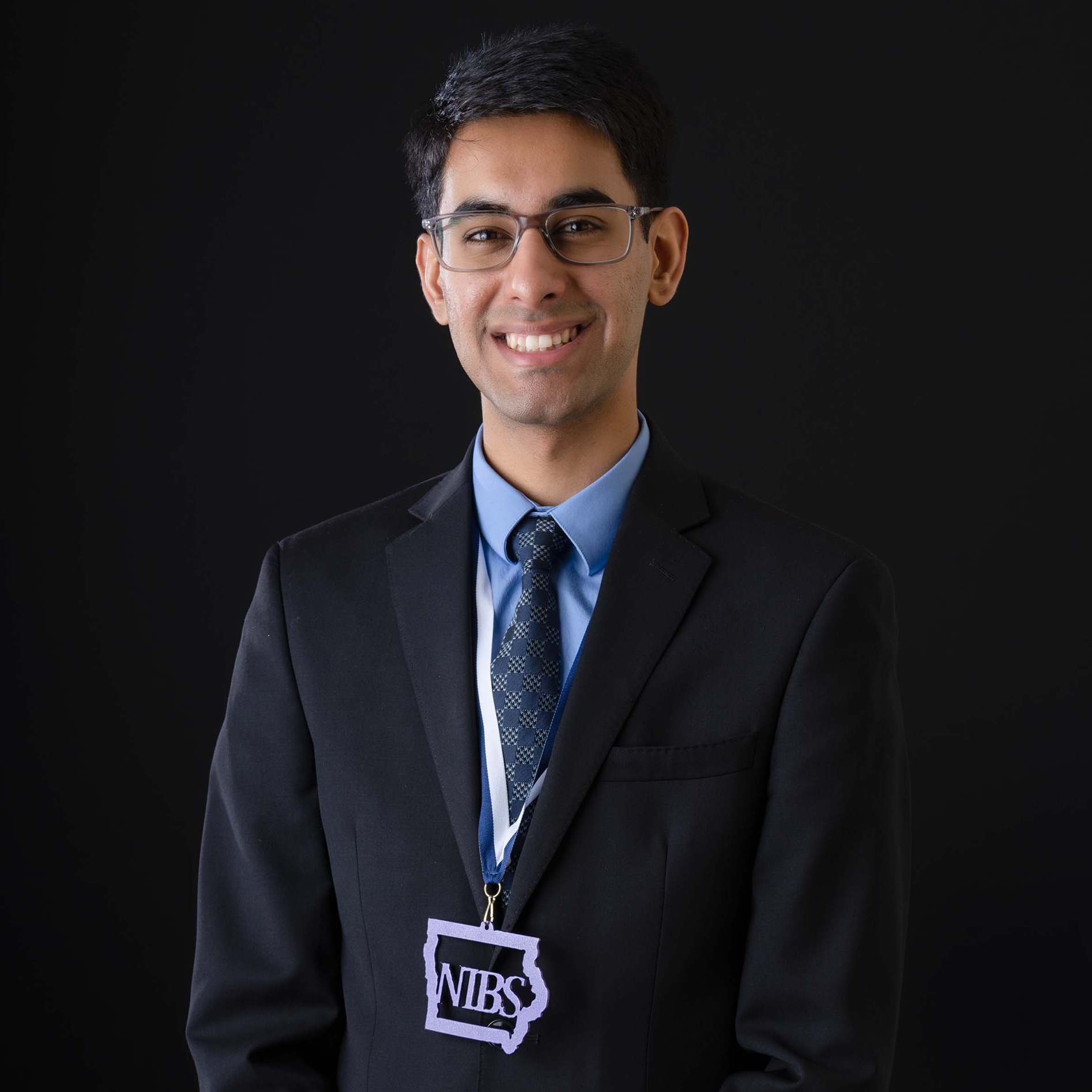 Agam Sharma smiles by a black background wearing a NIBS medal