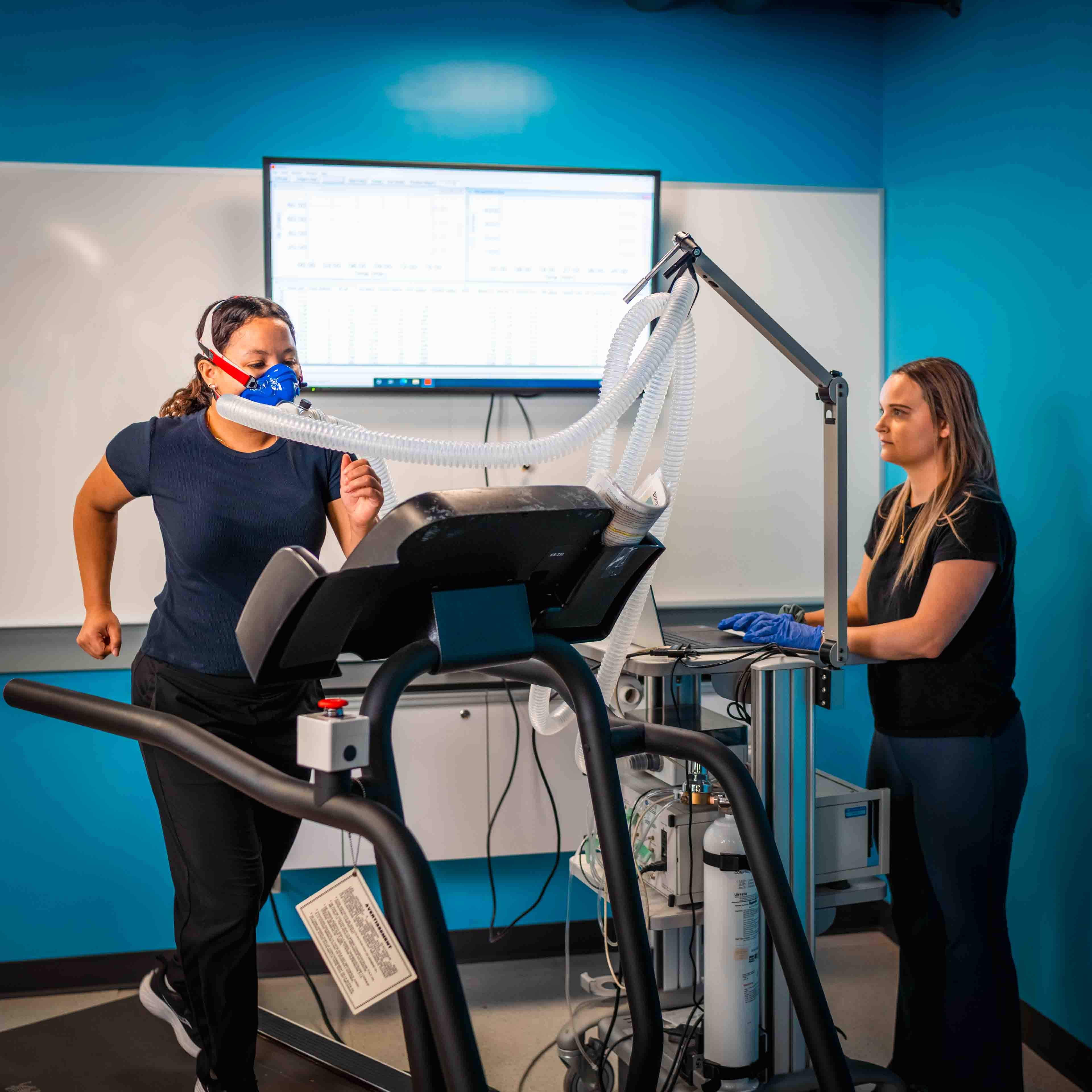 A woman runs on a treadmill with a mask in a lab