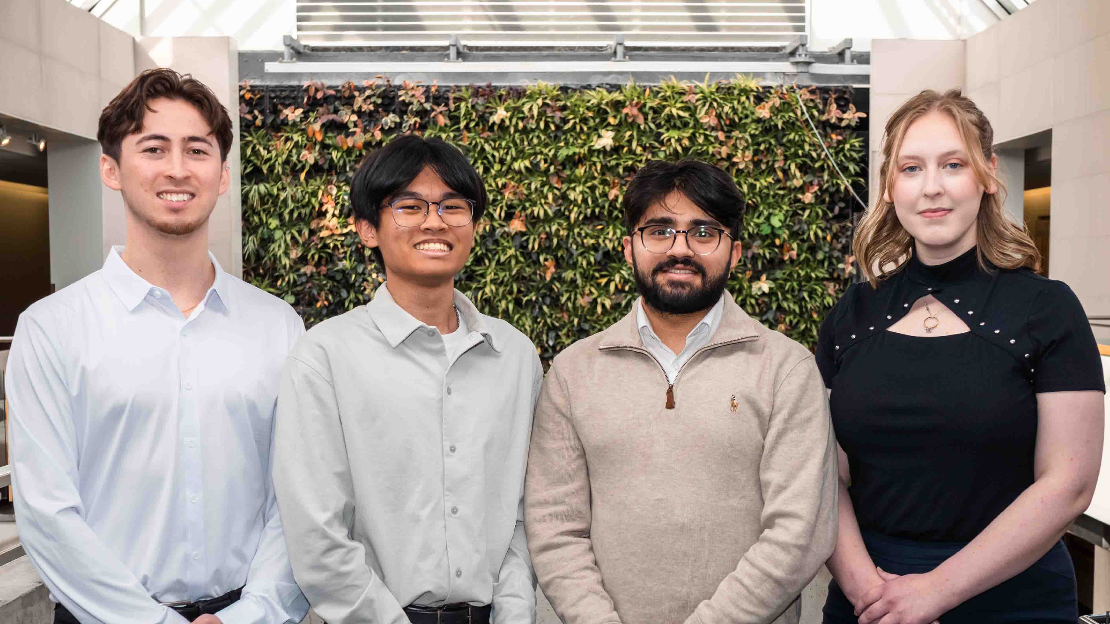 Four people stand in front of the plant wall