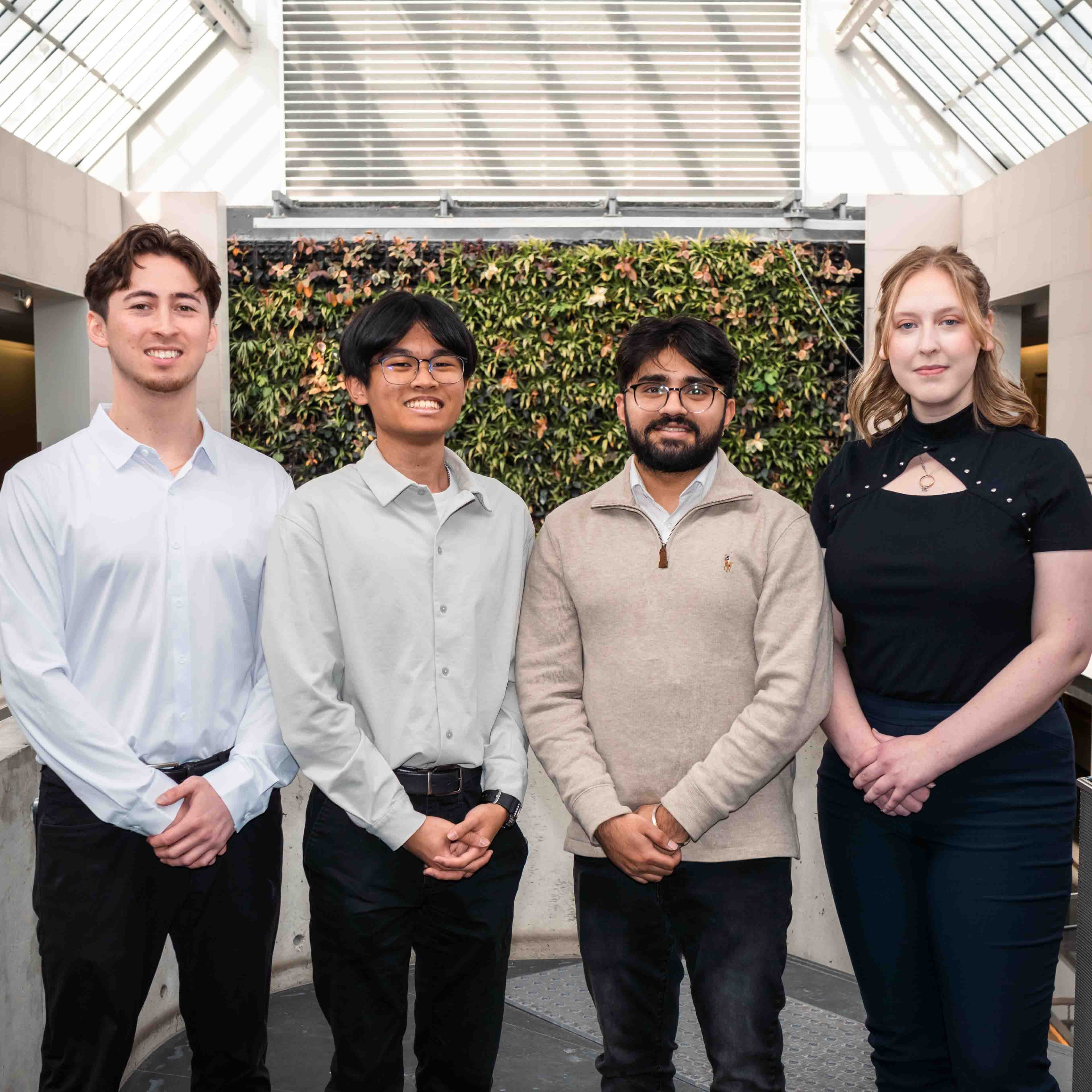 Four people stand in front of the plant wall