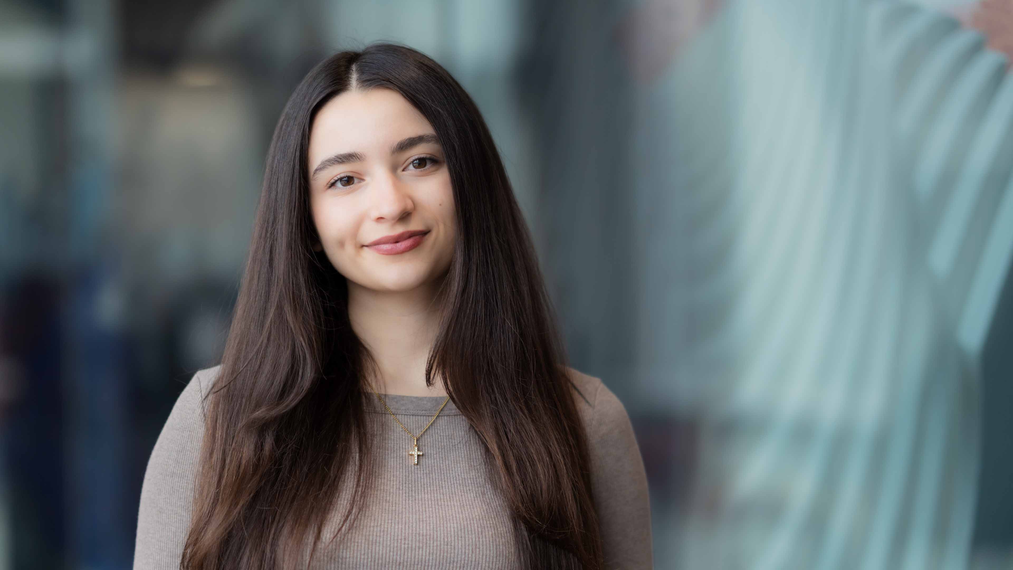 Melissa Kirakossian wears a taupe shirt with long brown hair, looks into the camera