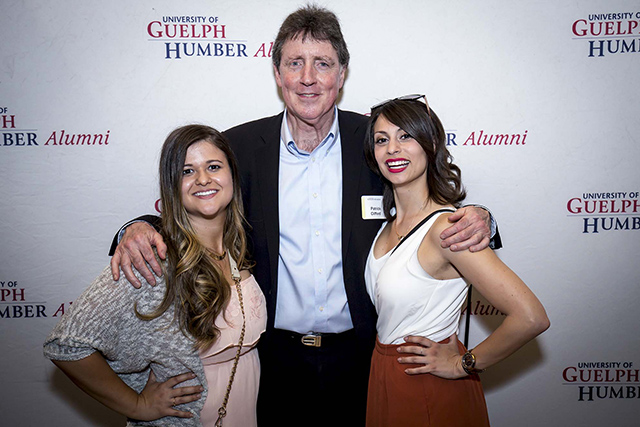 An instructor poses with two alumni