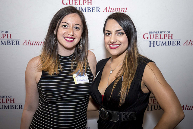 Two alumni pose in front of a UofGH backdrop