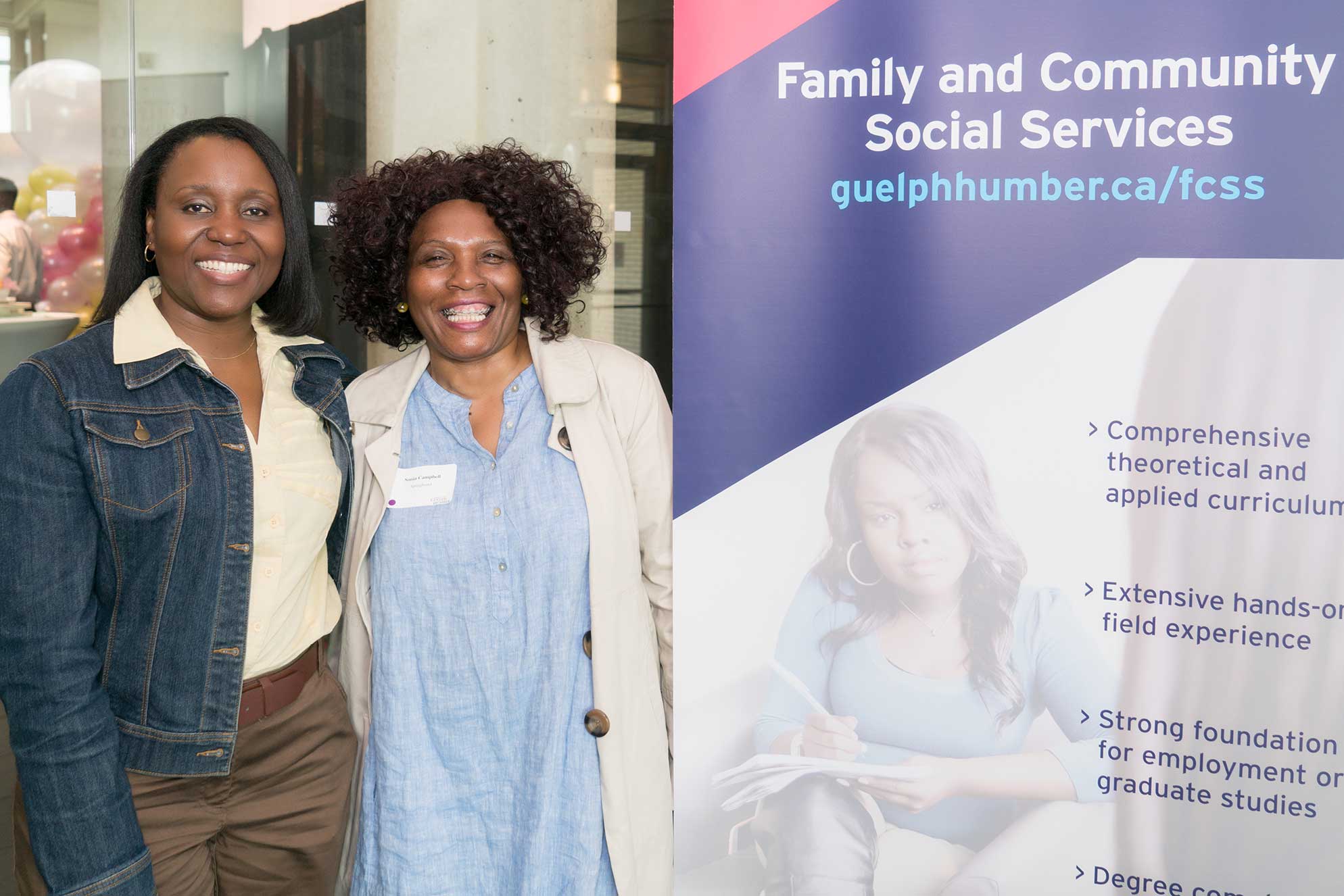 Two guests smile beside a sign for the FCSS program