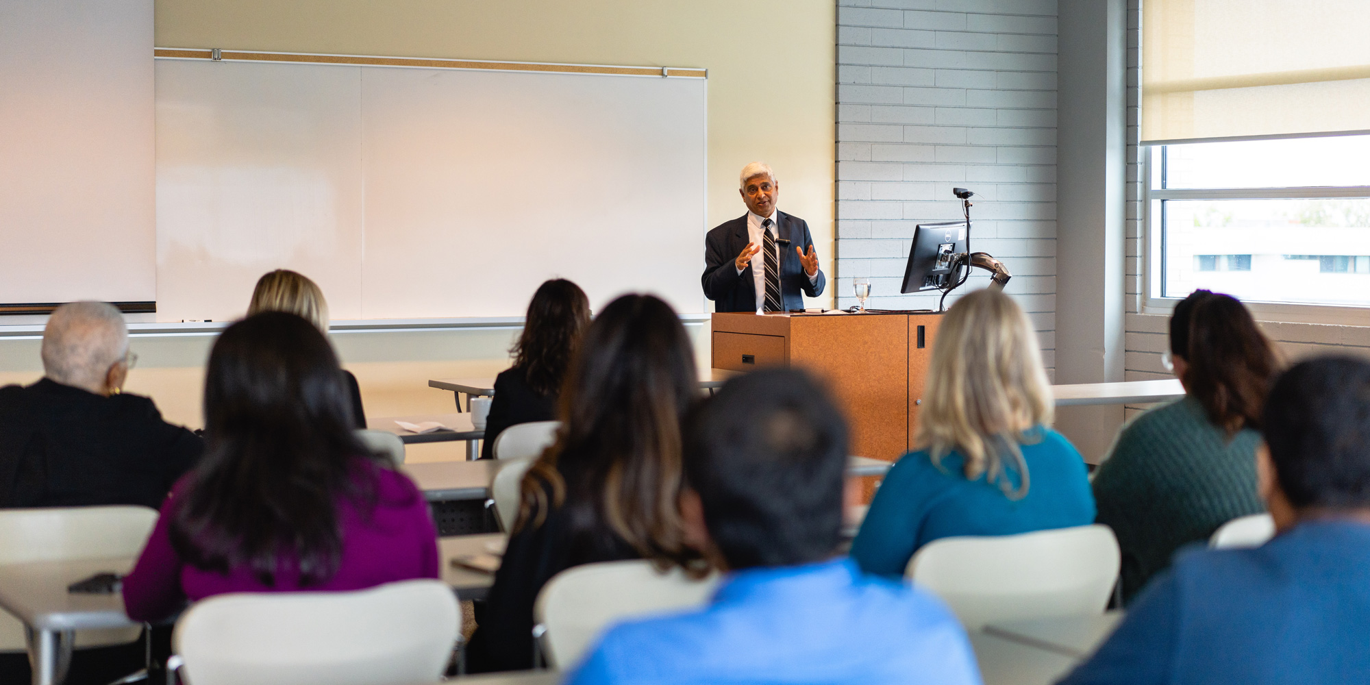 Vikas Swarup at the front of a classroom with several individuals sitting at tables in the foreground