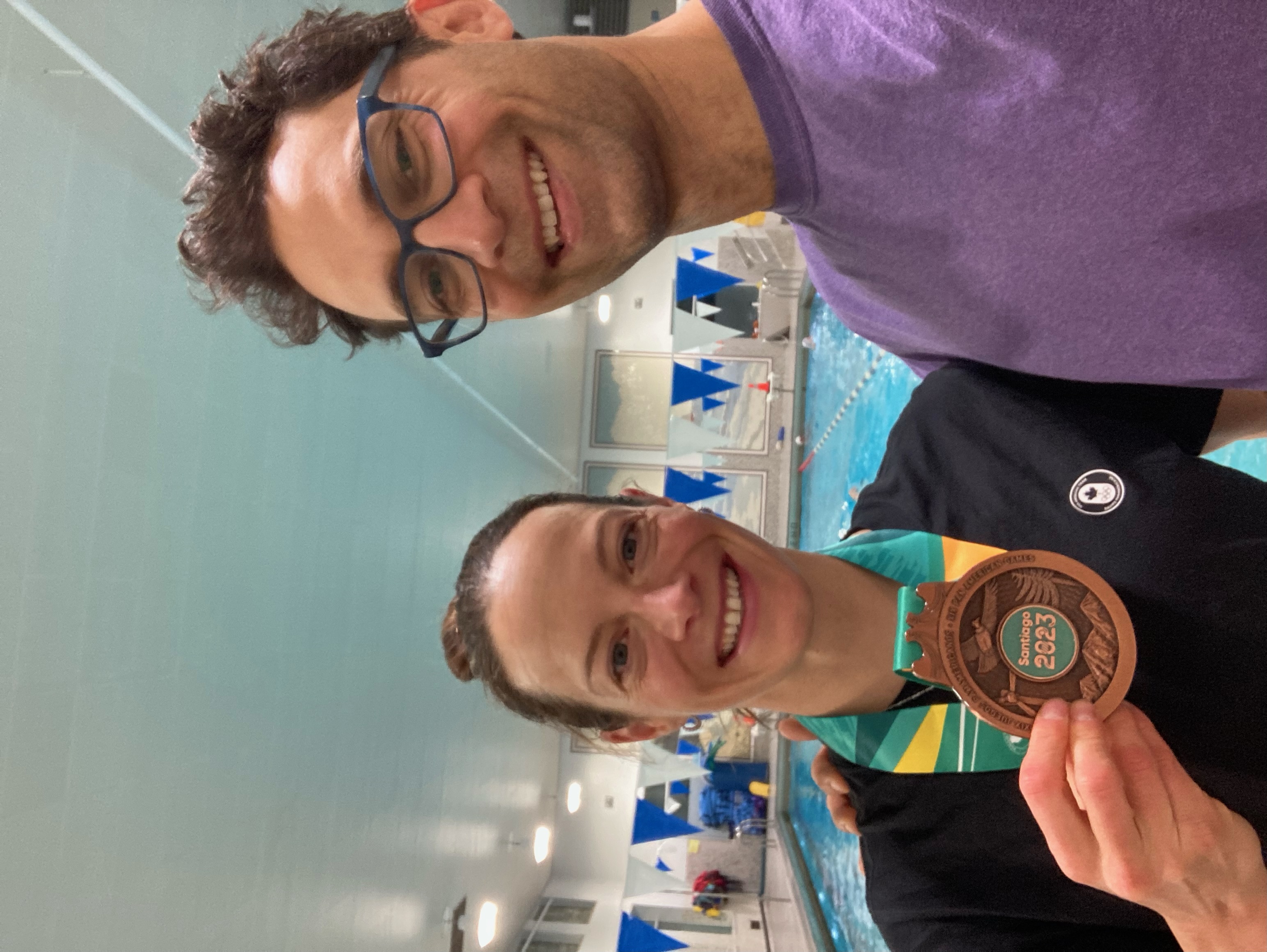 A selfie of two individuals where one individual is holding a bronze medal