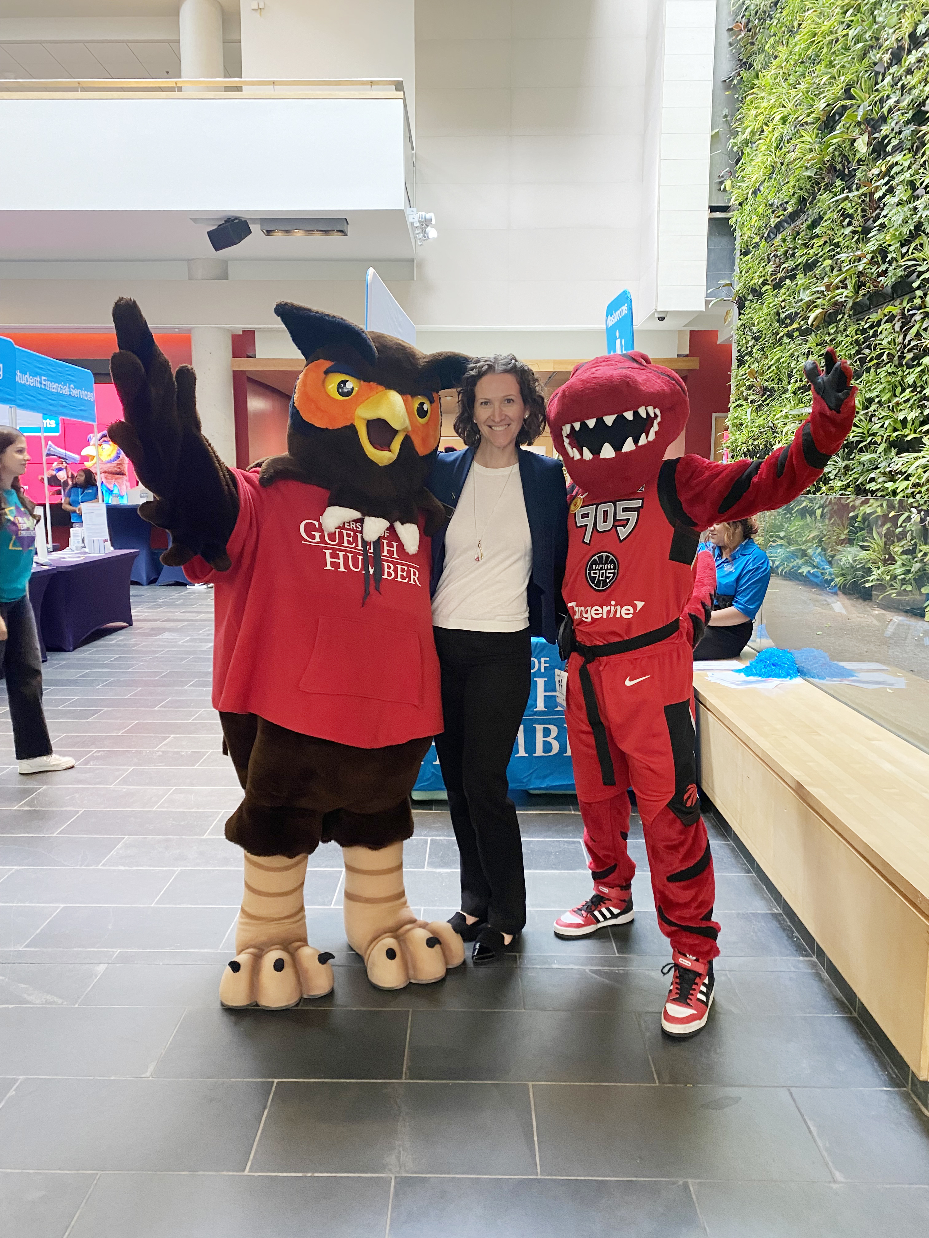 Dr. Leslie Auger standing with Swoop, the University of Guelph-Humber great horned owl mascot and Stripes, Raptors 905 masoct