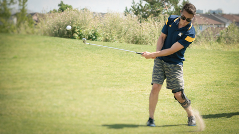 Photo of UofGH alumni striking golf ball with plume of dirt rising from grass