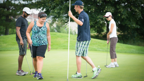 Photo of 4 UofGH alumni gathering around flag on golf green