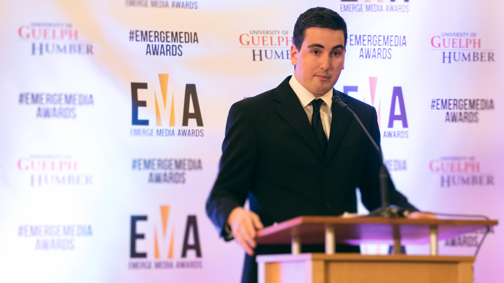 Man on stage, giving a speech with both hands on podium_