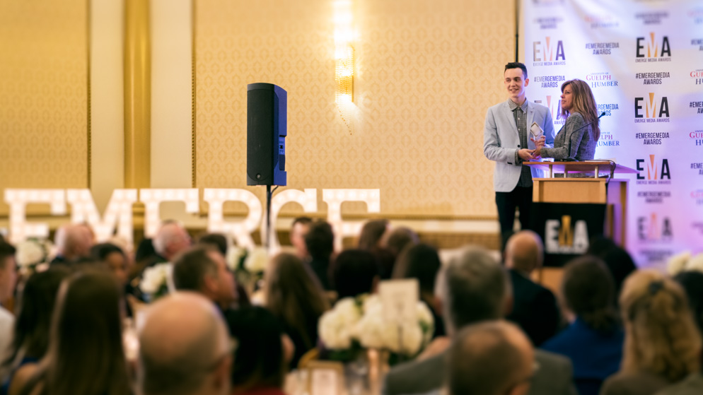 Male student receiving award at podium with seated crowd in foreground_