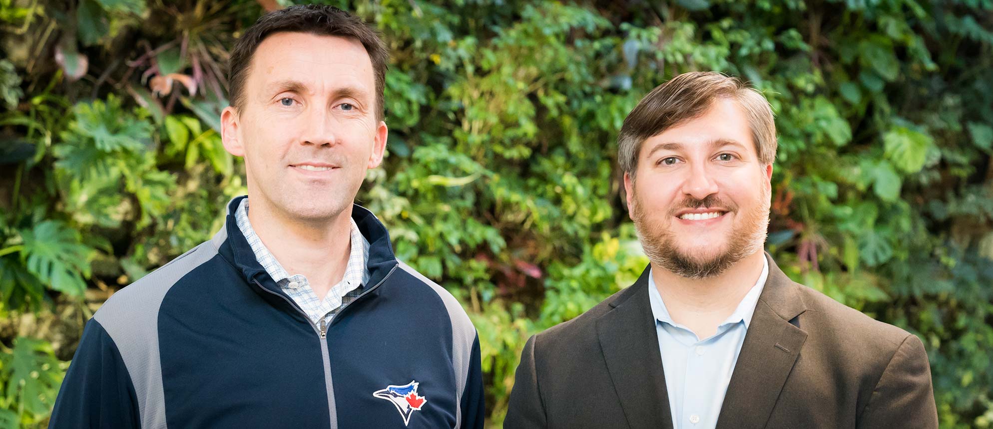 Jay Stenhouse and Heath Applebaum smiling by the plant wall.