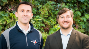 Two men smiling infront of plant wall